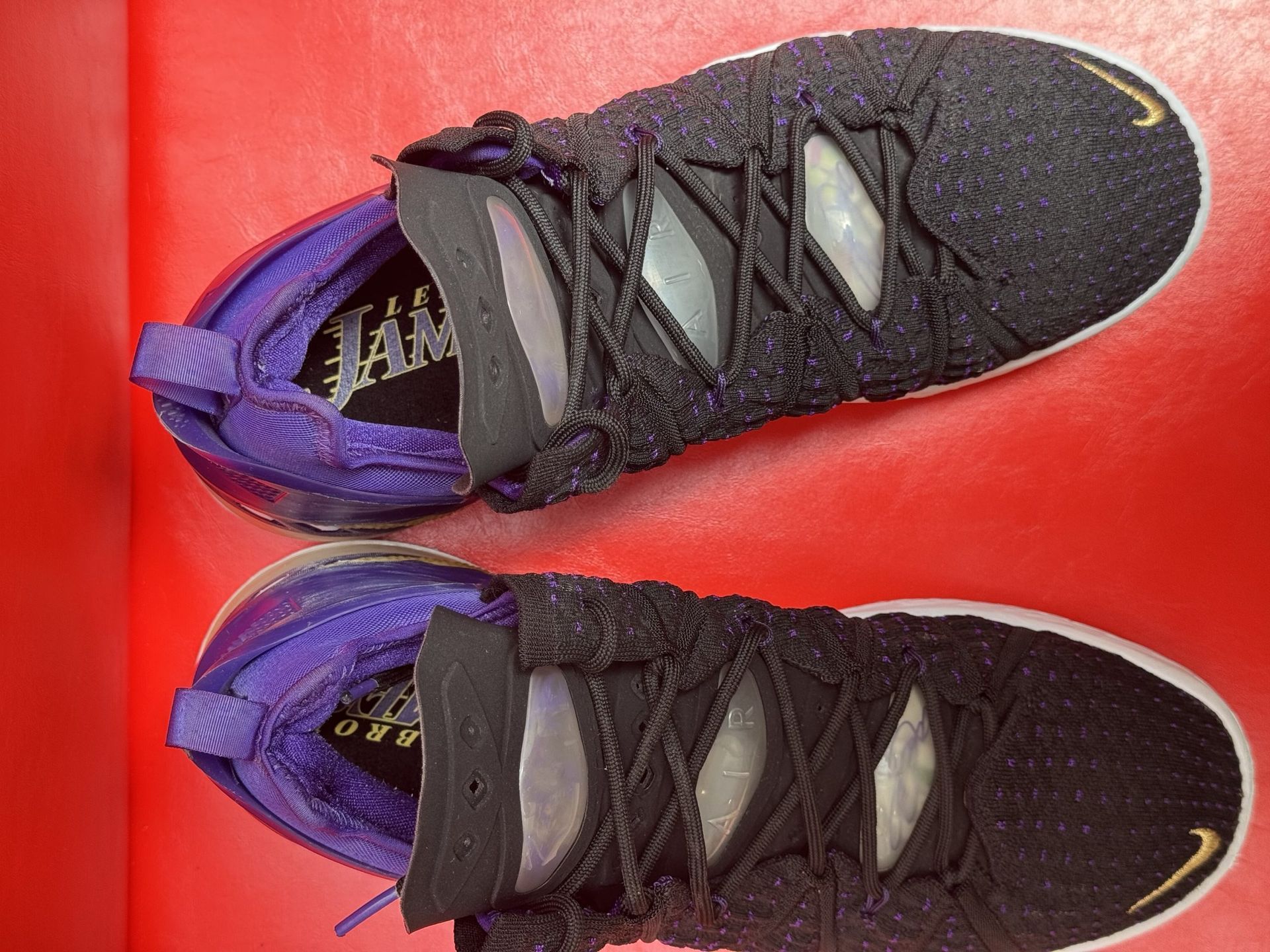 Black and purple Nike LeBron 18 basketball sneakers with white soles, set against a red background.