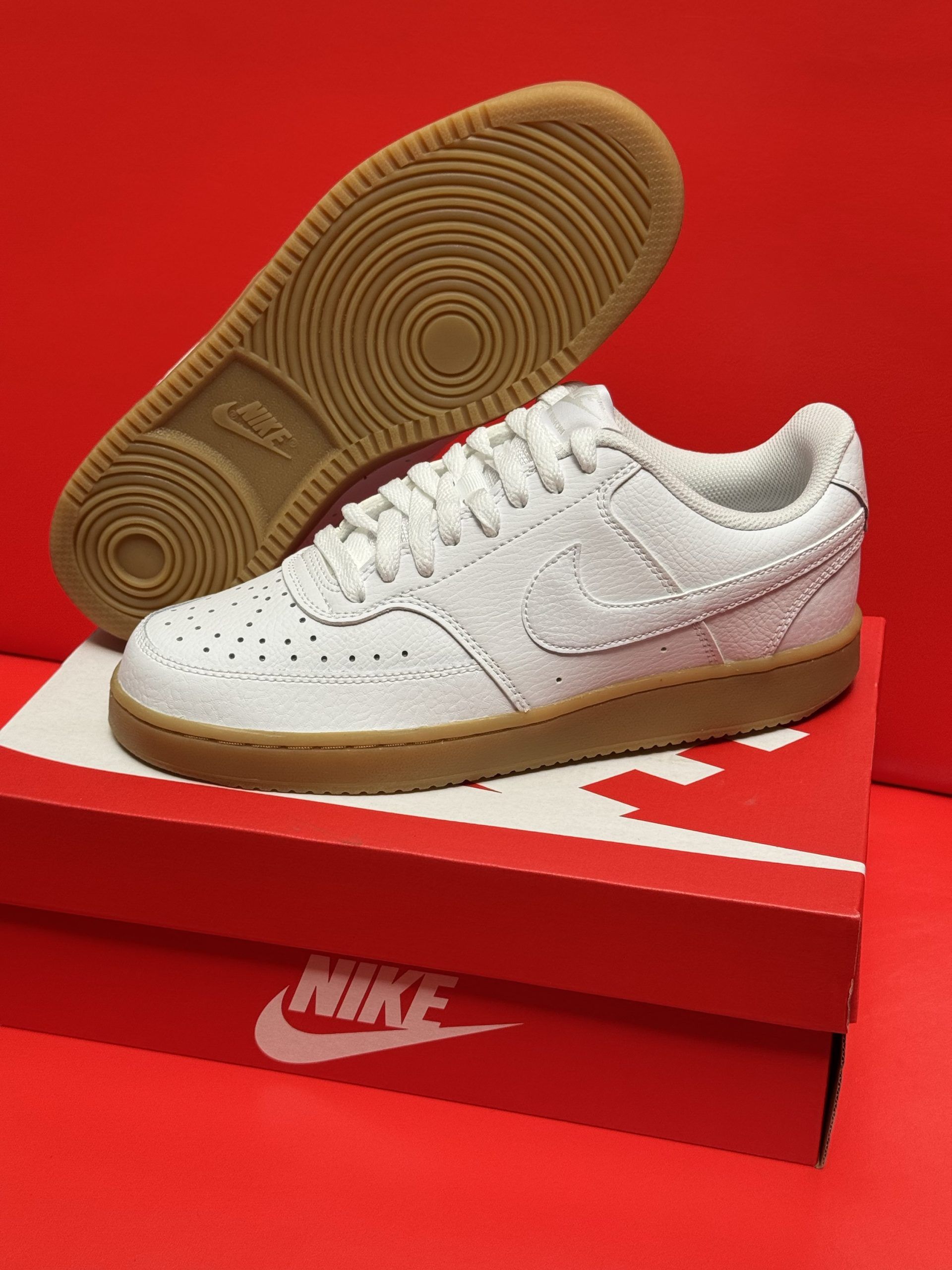 White Nike Court Vision sneakers on a red Nike box, with a brown sole and the shoe's sole visible.