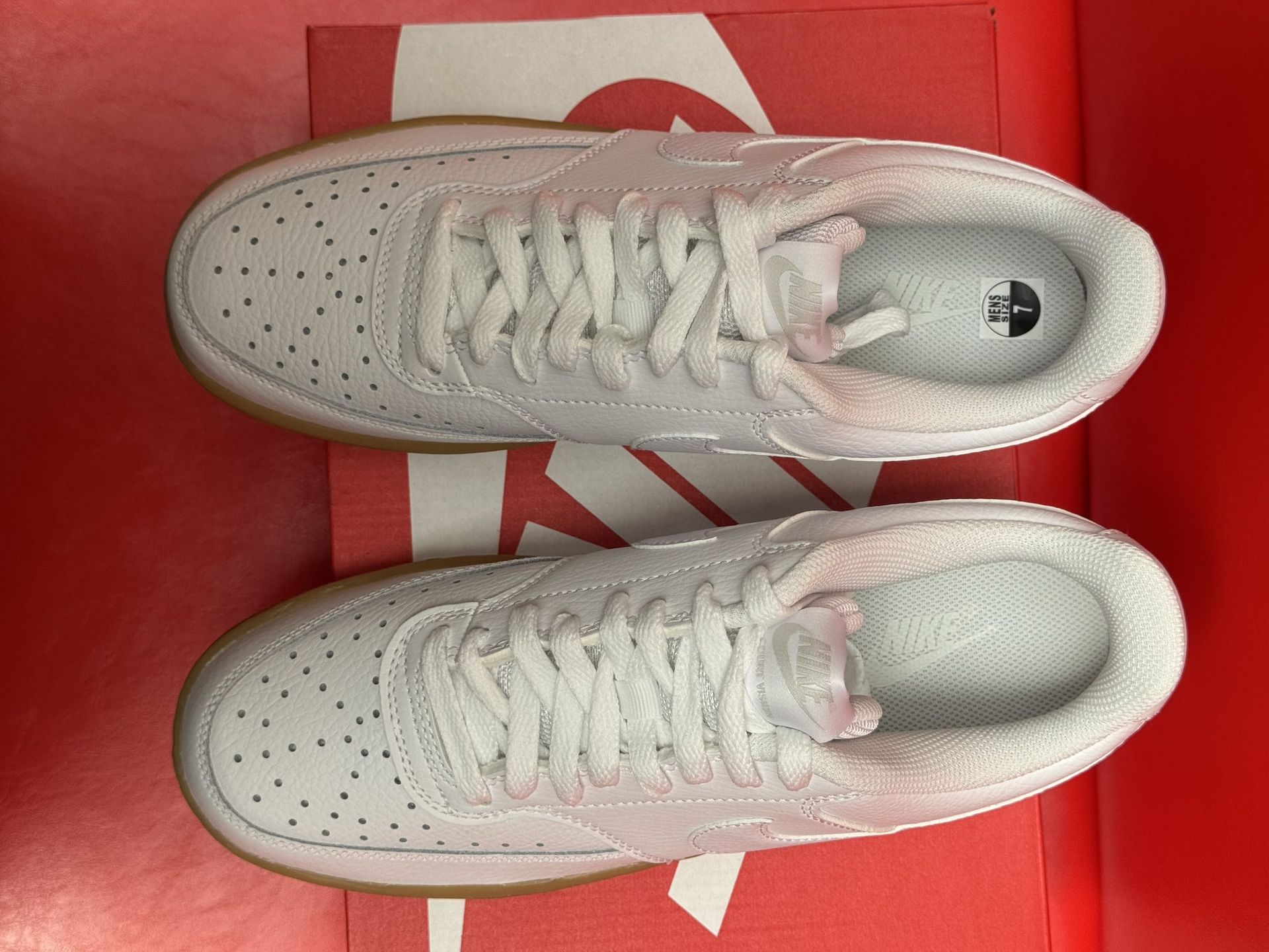 White Nike Court Vision sneakers on a red Nike box, with a brown sole and the shoe's sole visible.