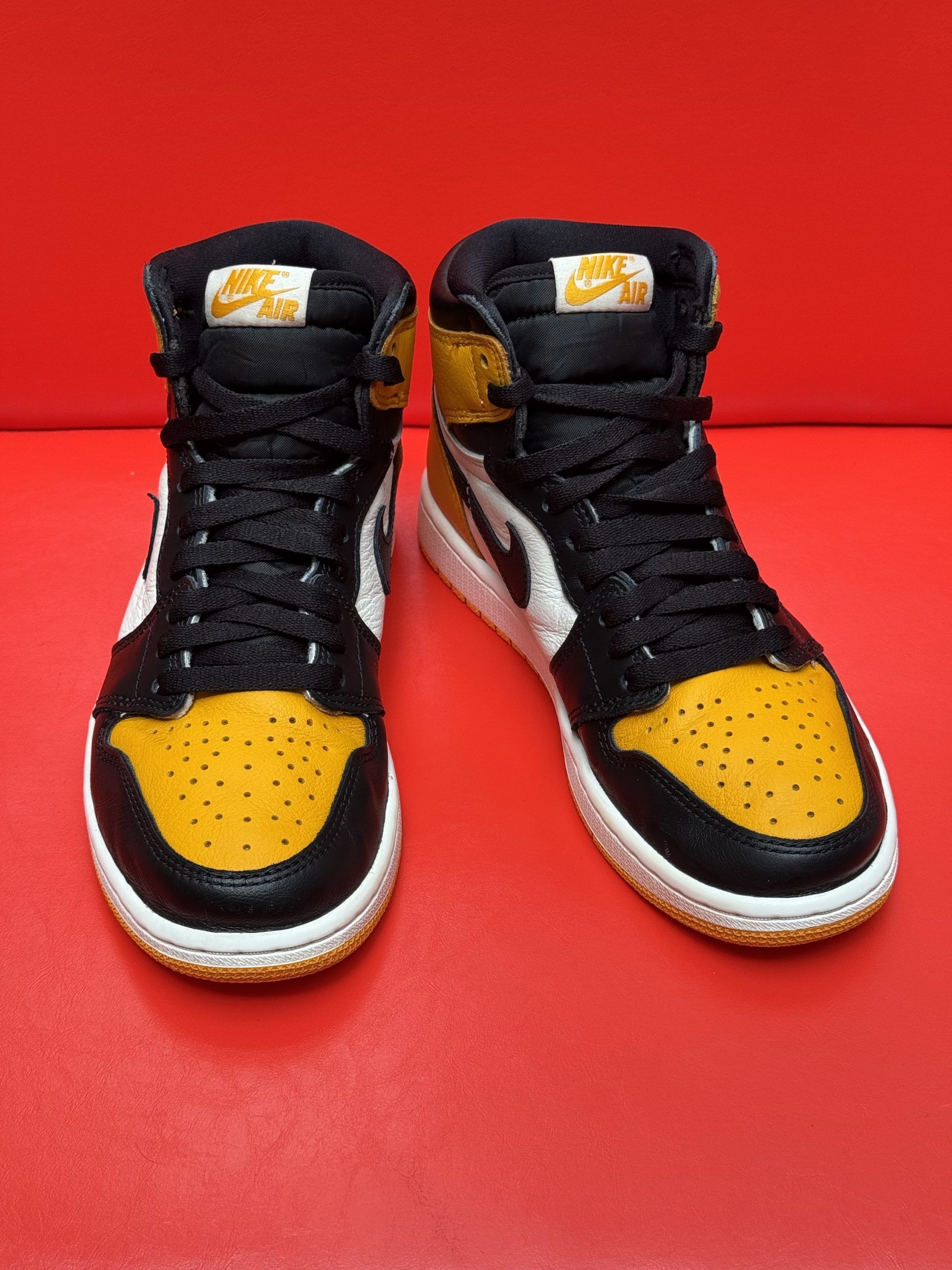 Yellow, black, and white high-top Air Jordan 1 sneaker with a visible yellow sole against a red backdrop.