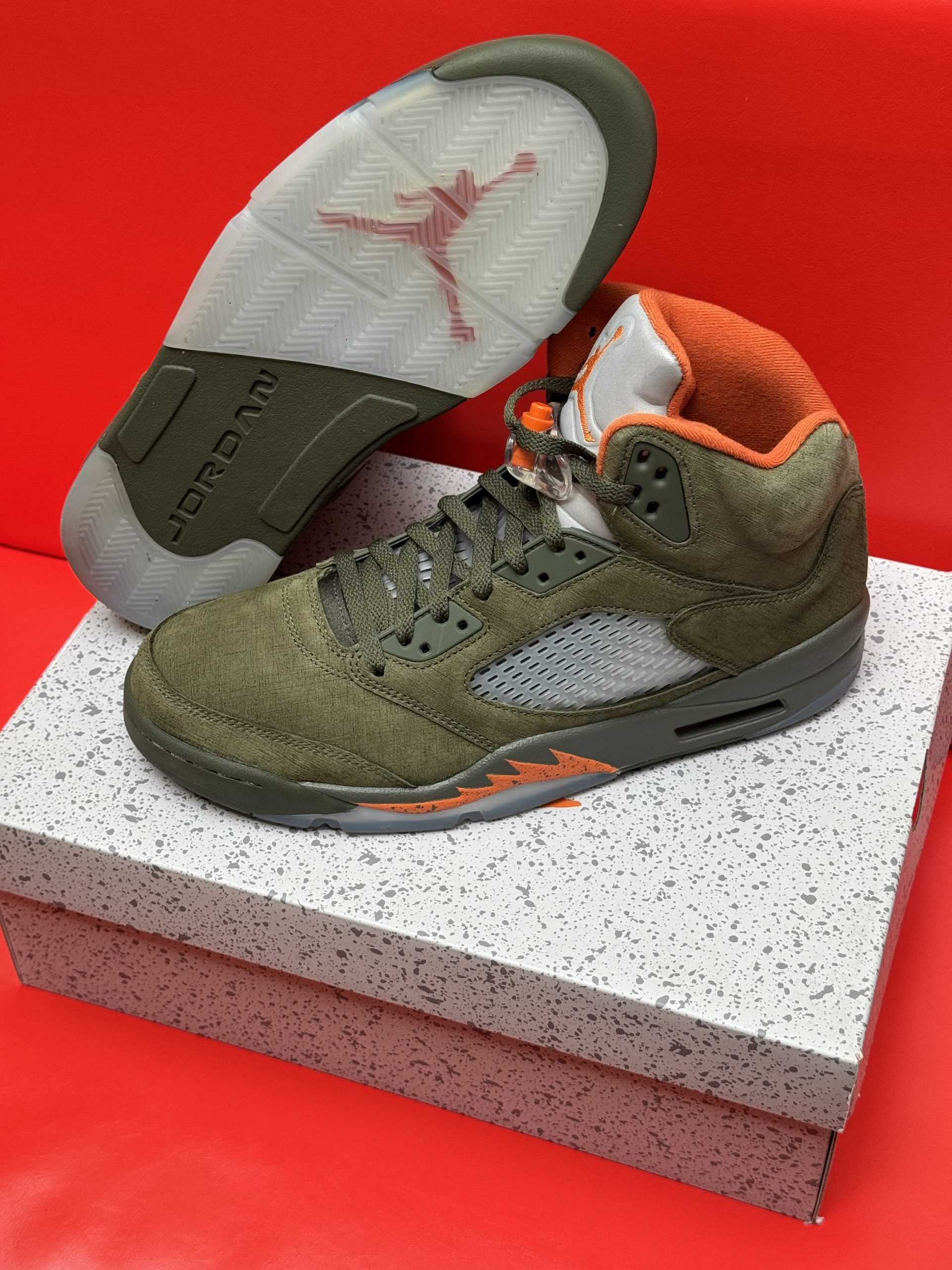 Olive green and orange Air Jordan 5 sneakers with a visible sole on a speckled box.