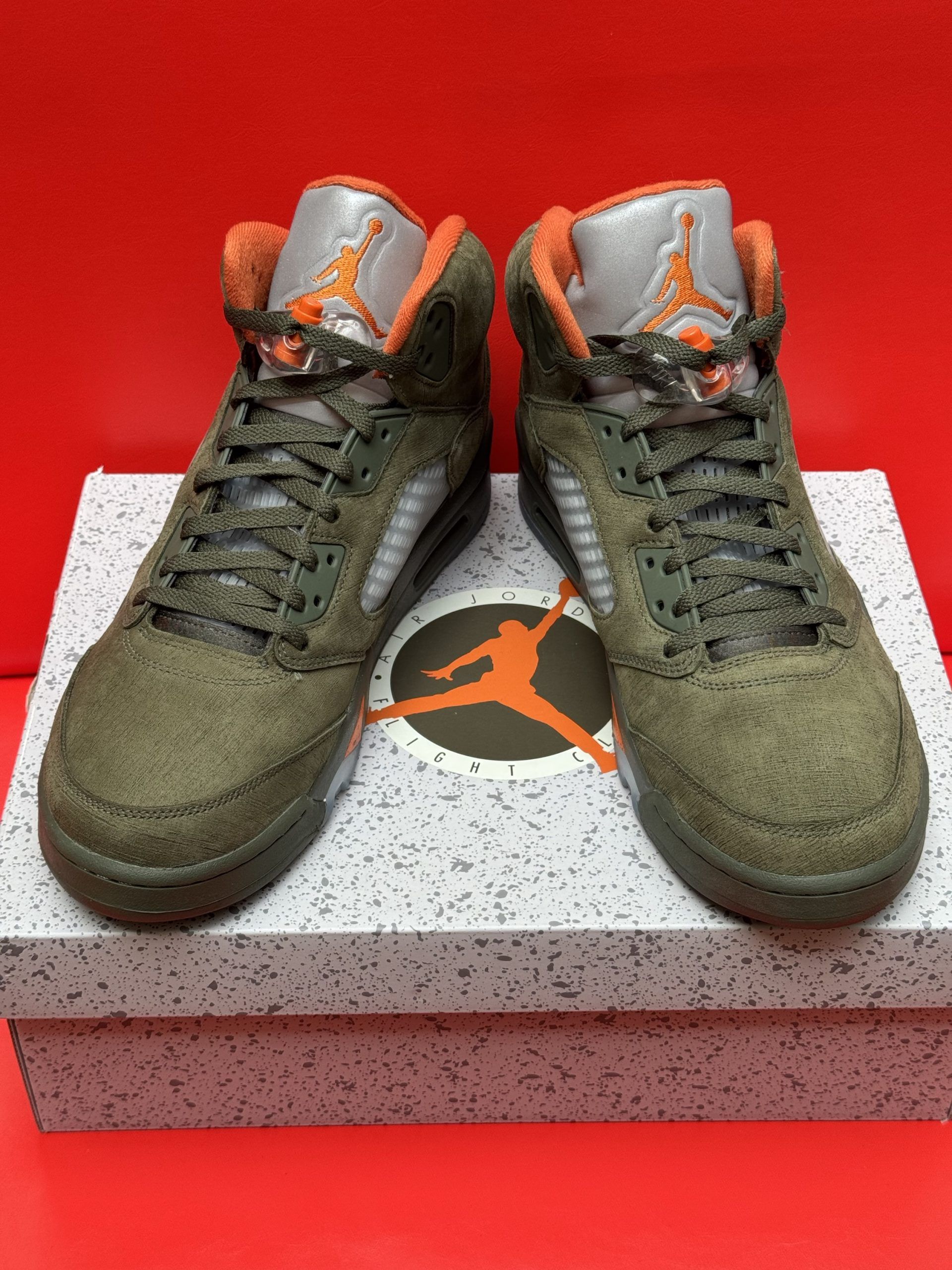Olive green and orange Air Jordan 5 sneakers with a visible sole on a speckled box.