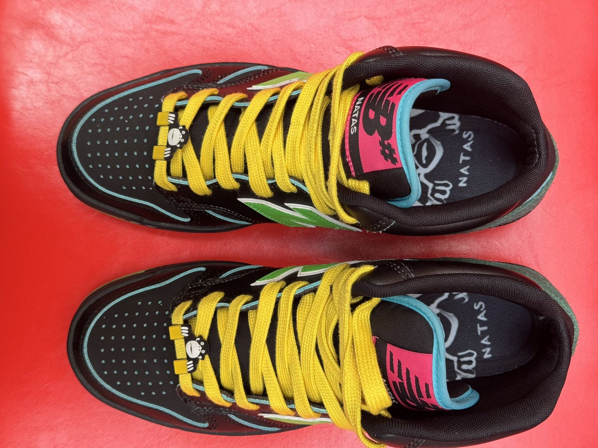 Black and green New Balance high-top sneaker with yellow laces, sole visible on red background.