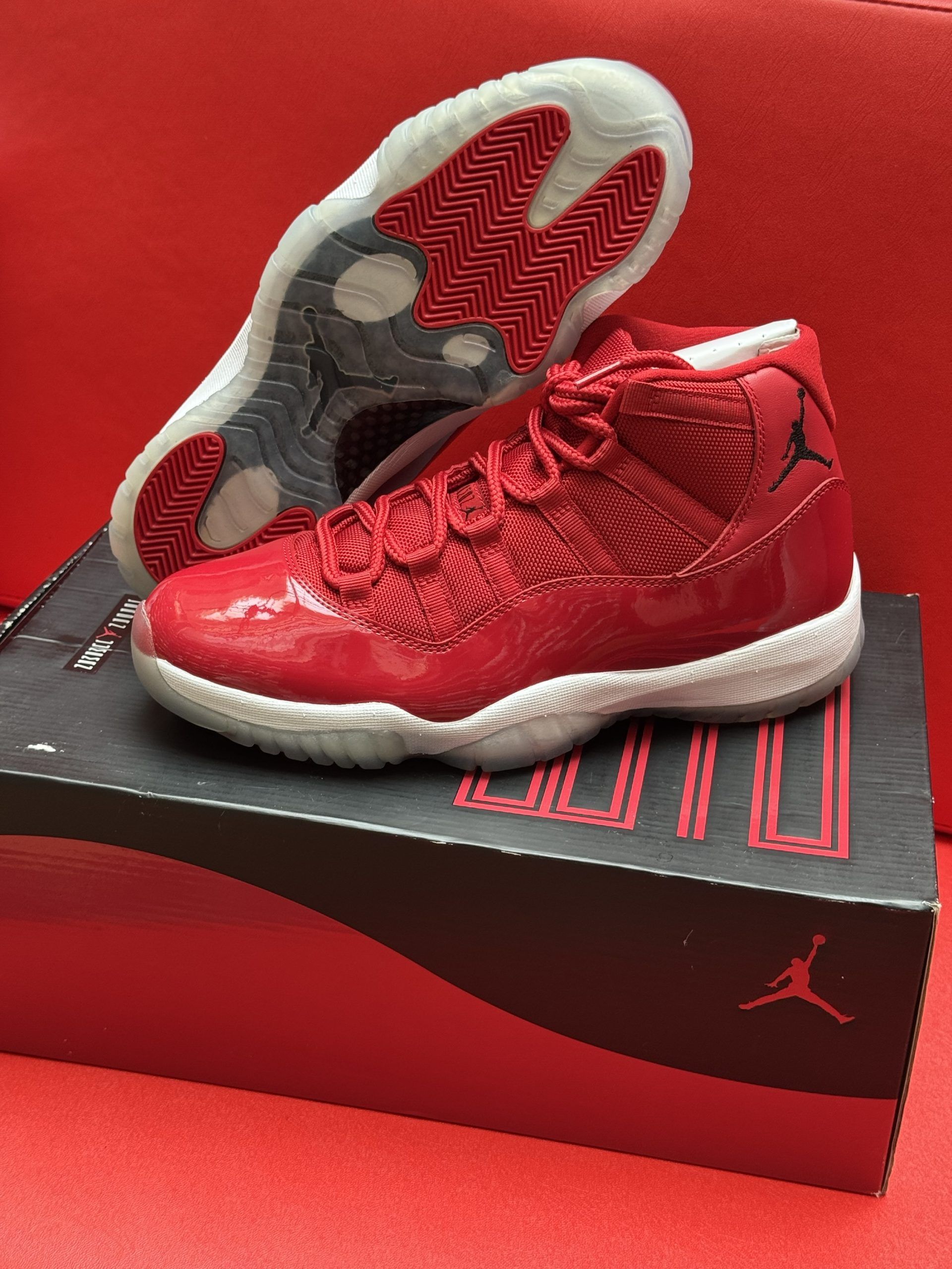Red Air Jordan 11 sneakers on a box, sole up, red background.
