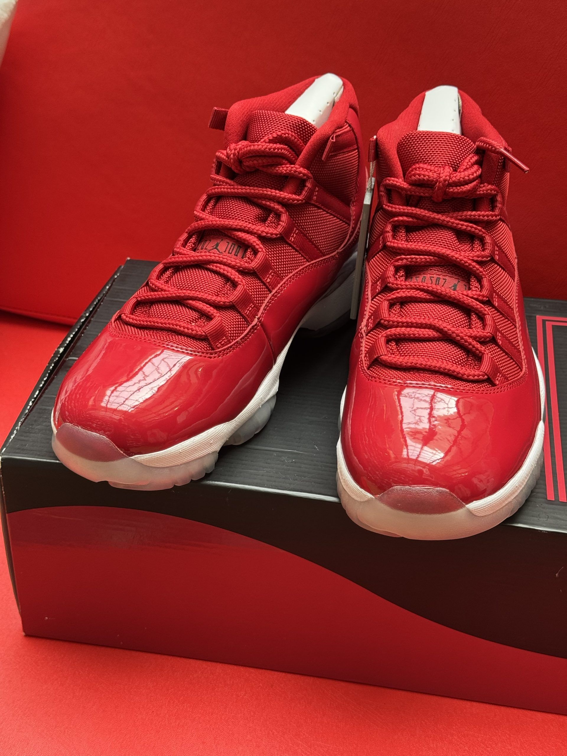 Red Air Jordan 11 sneakers on a box, sole up, red background.
