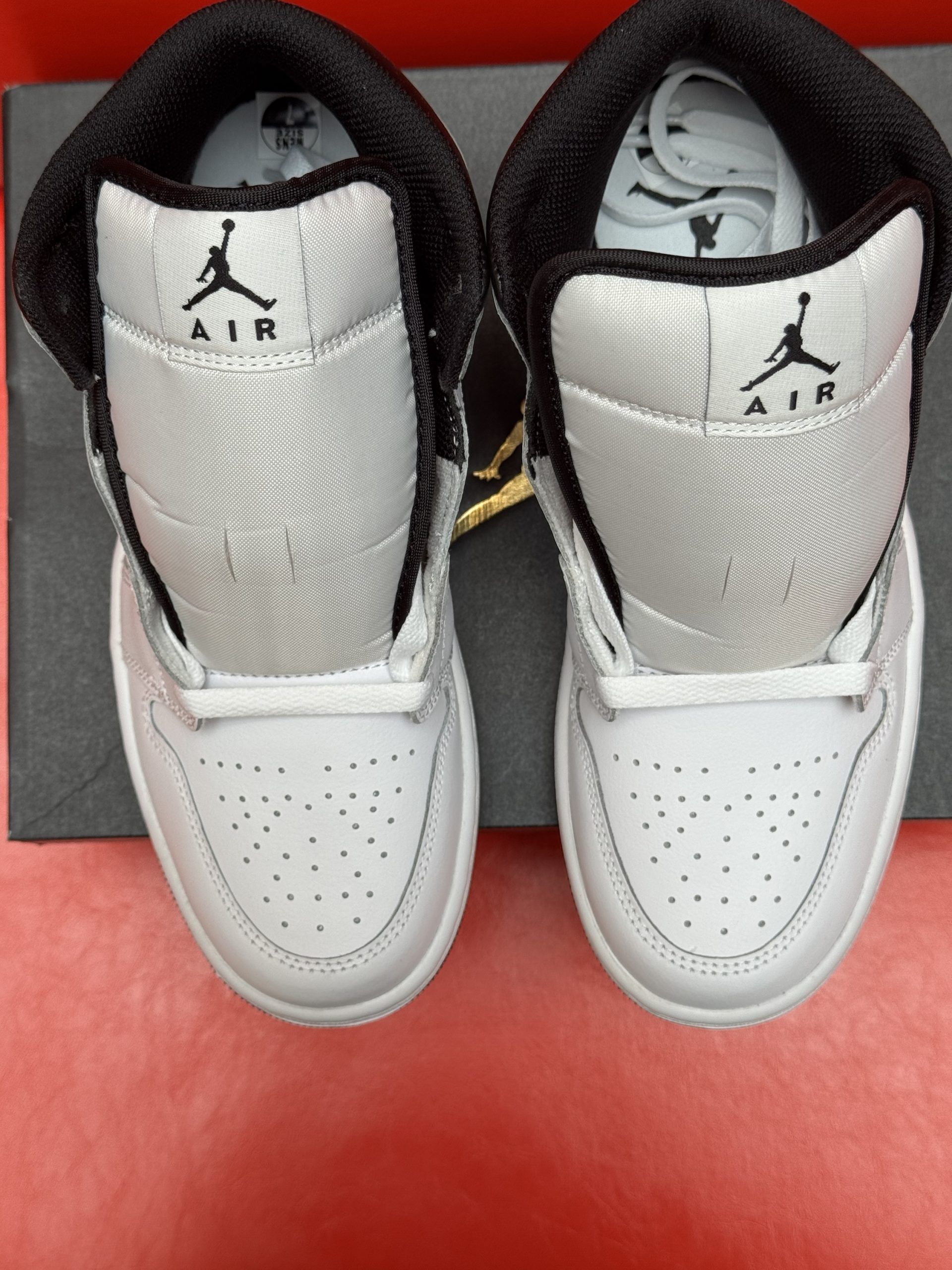 White and black Air Jordan 1 sneaker on a black box, sole visible. Red background.