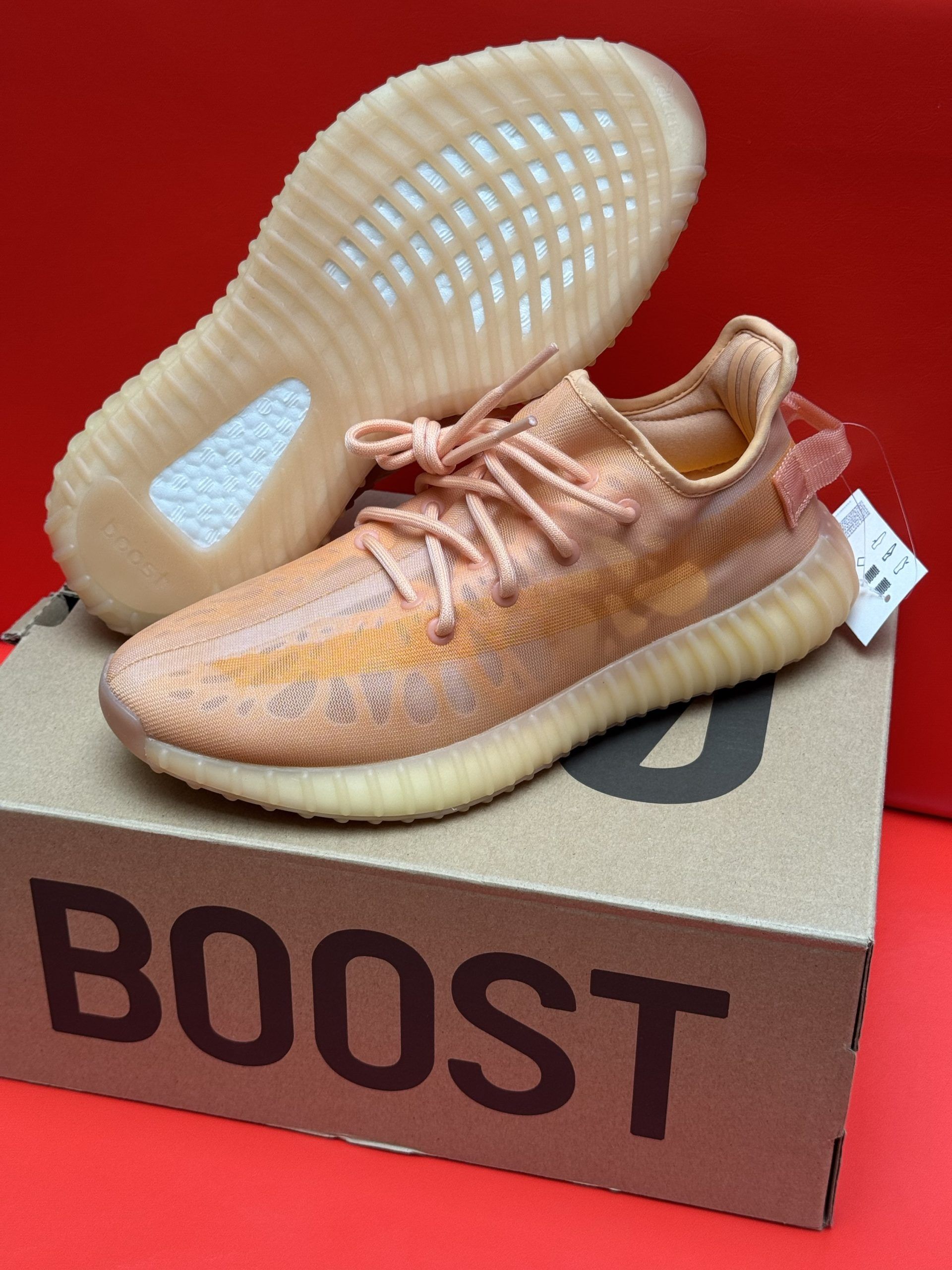 Adidas Yeezy Boost 350 V2 sneakers in orange and tan colors, one on top of the other, sitting on the original box.