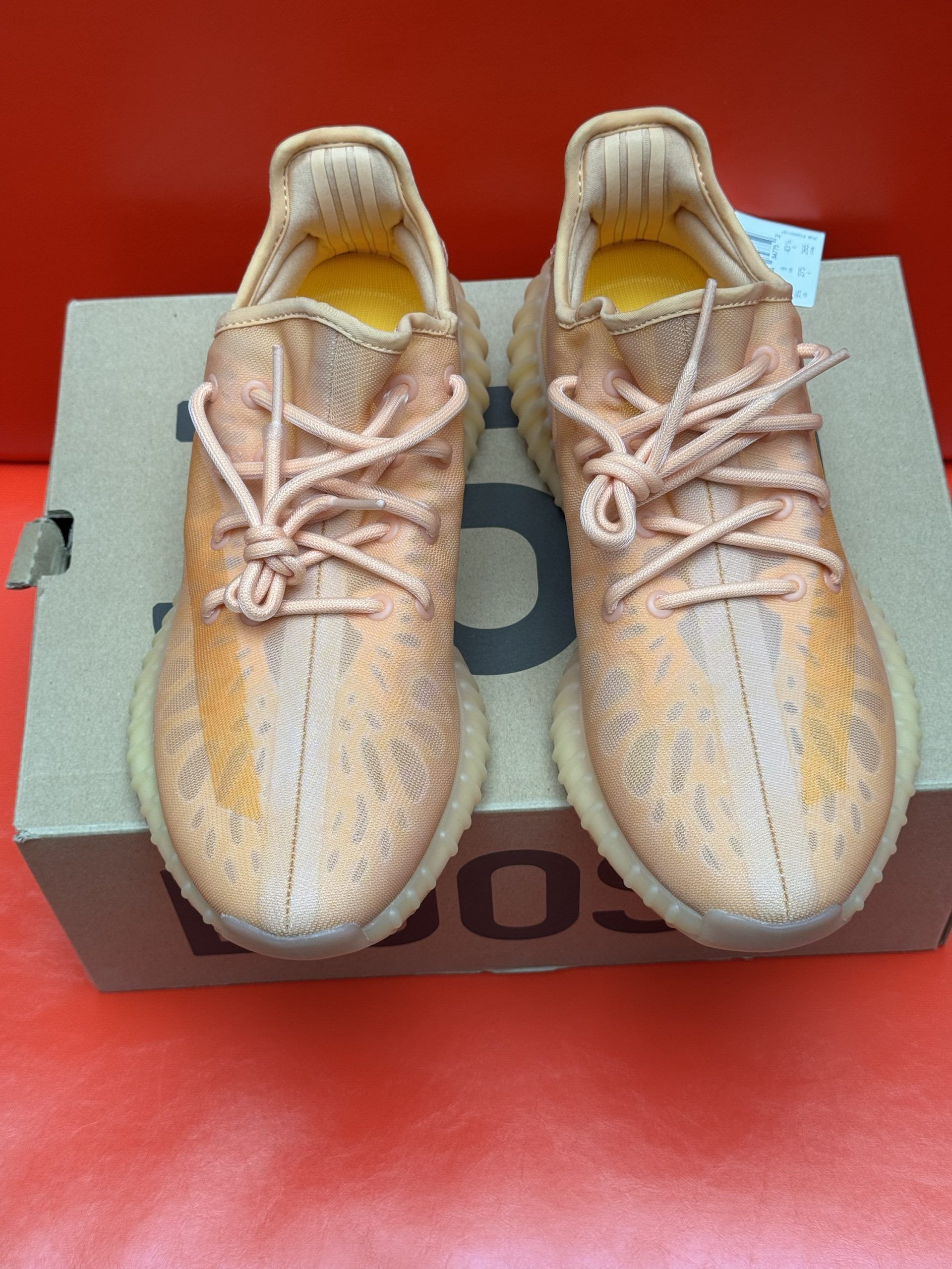 Adidas Yeezy Boost 350 V2 sneakers in orange and tan colors, one on top of the other, sitting on the original box.