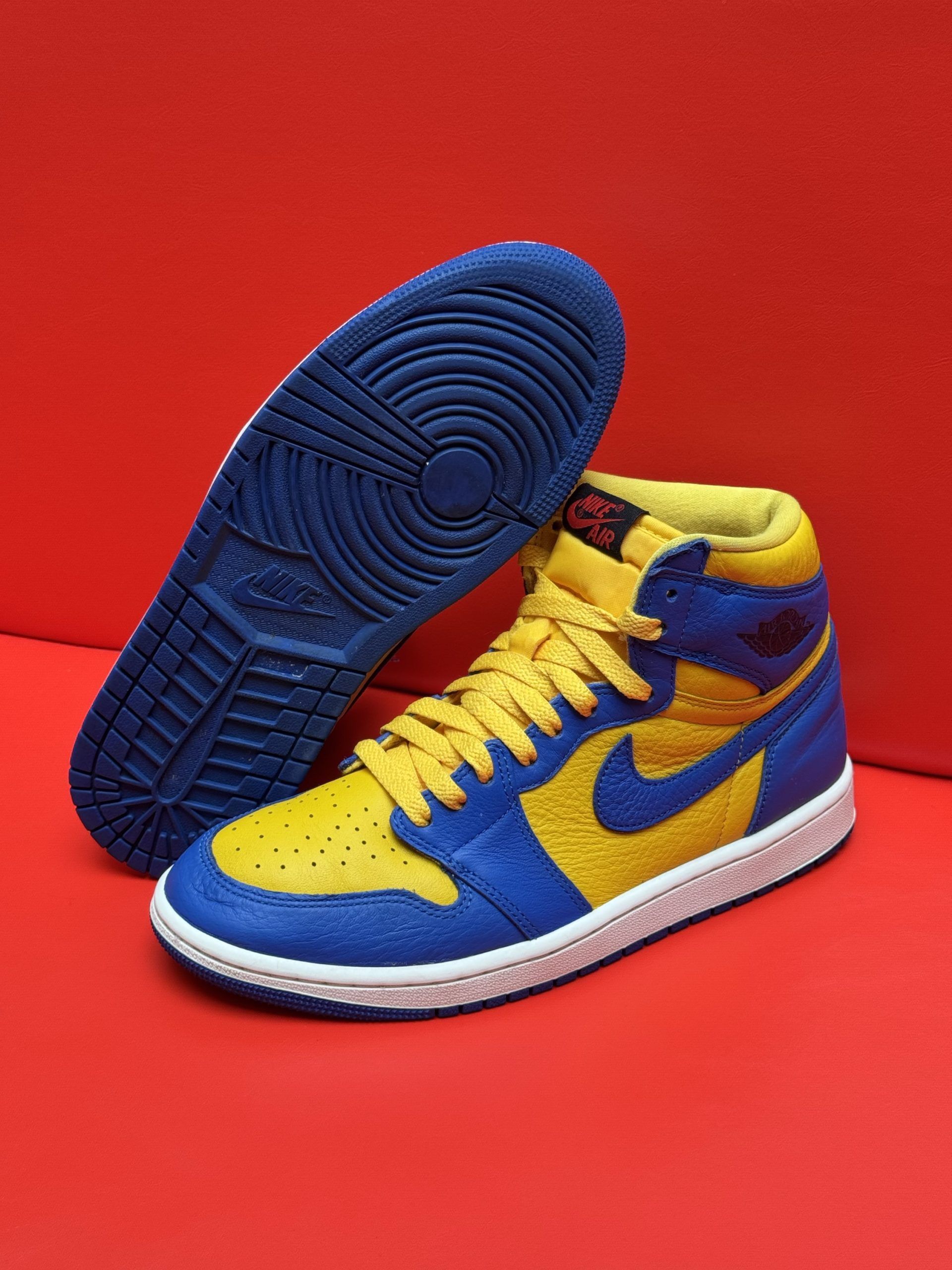 Blue and yellow high-top sneaker with a white sole, and blue sole is off to the side, set on a red surface.