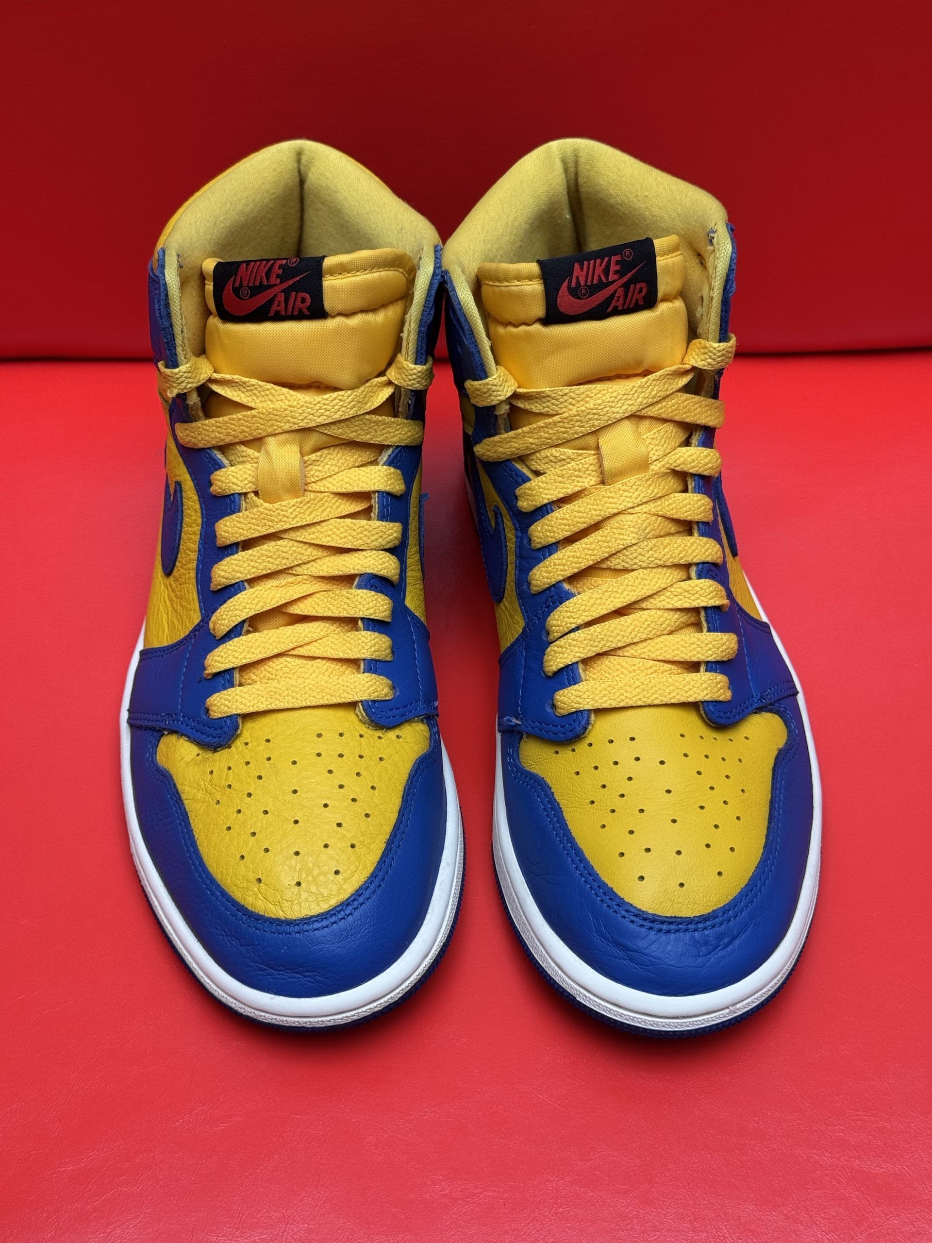Blue and yellow high-top sneaker with a white sole, and blue sole is off to the side, set on a red surface.