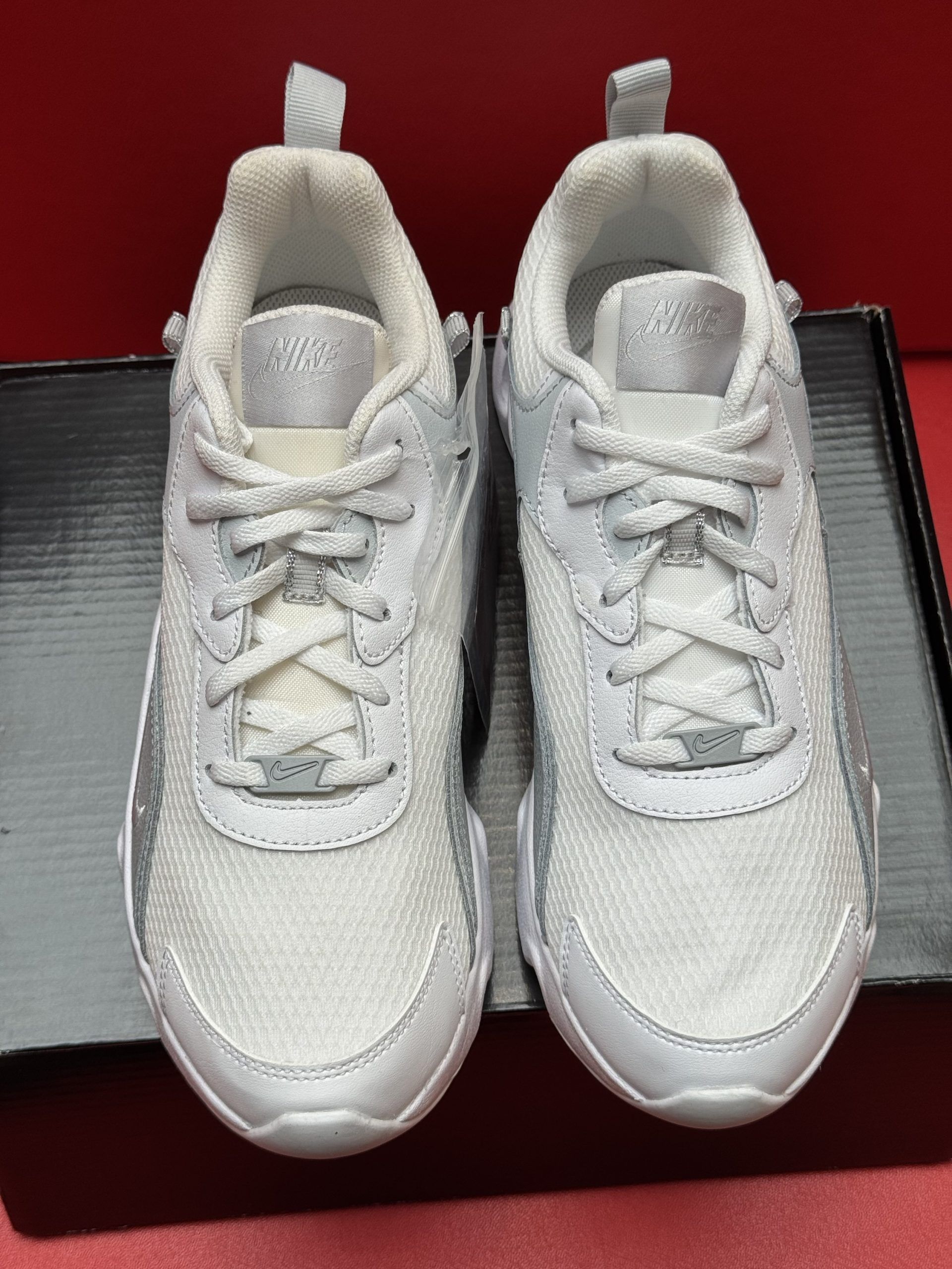 White sneakers on a black box, one showing its wavy sole. Red background.