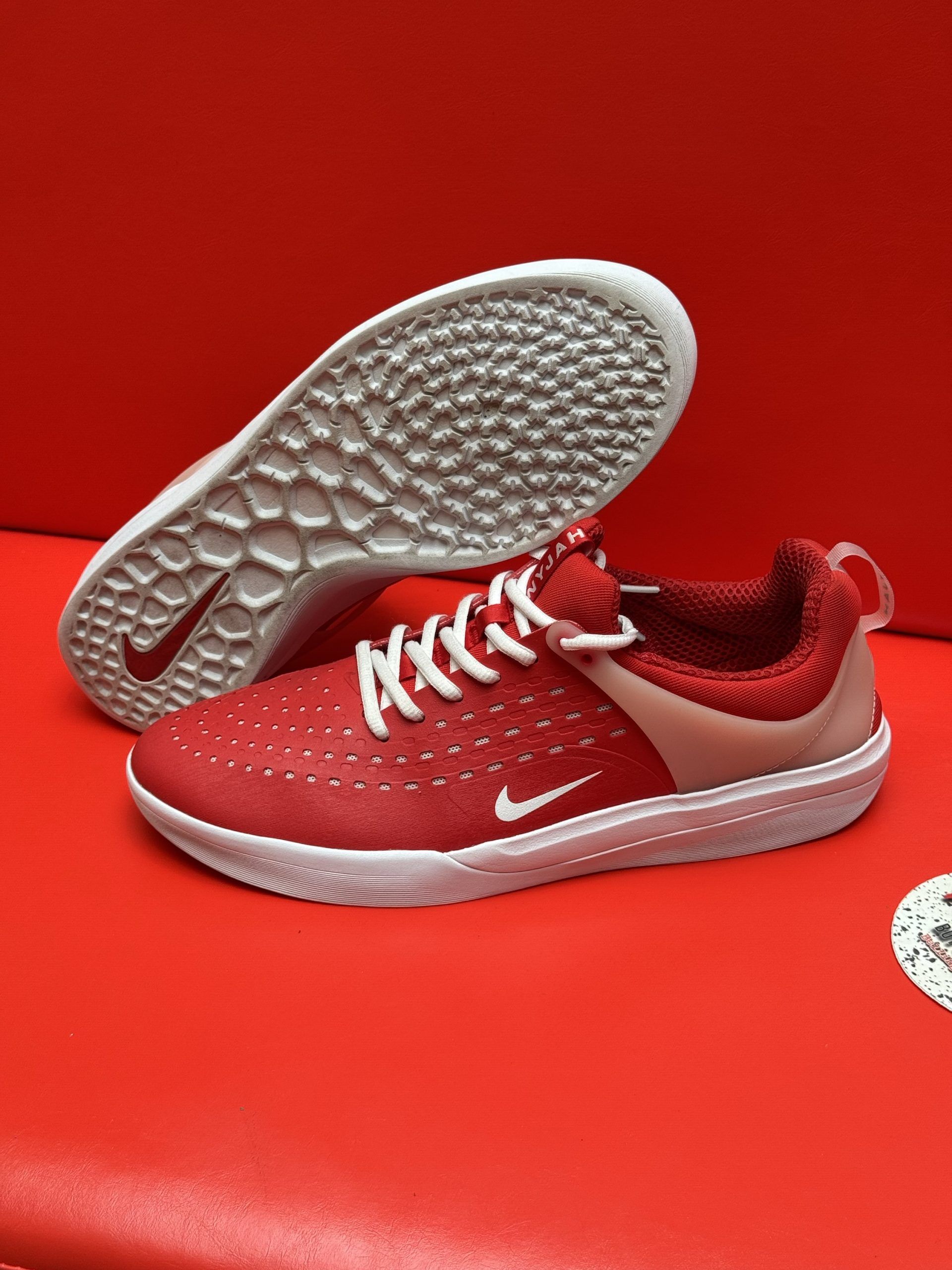 Red Nike shoes, one lying on its sole, against a red background. White sole, laces, and swoosh.