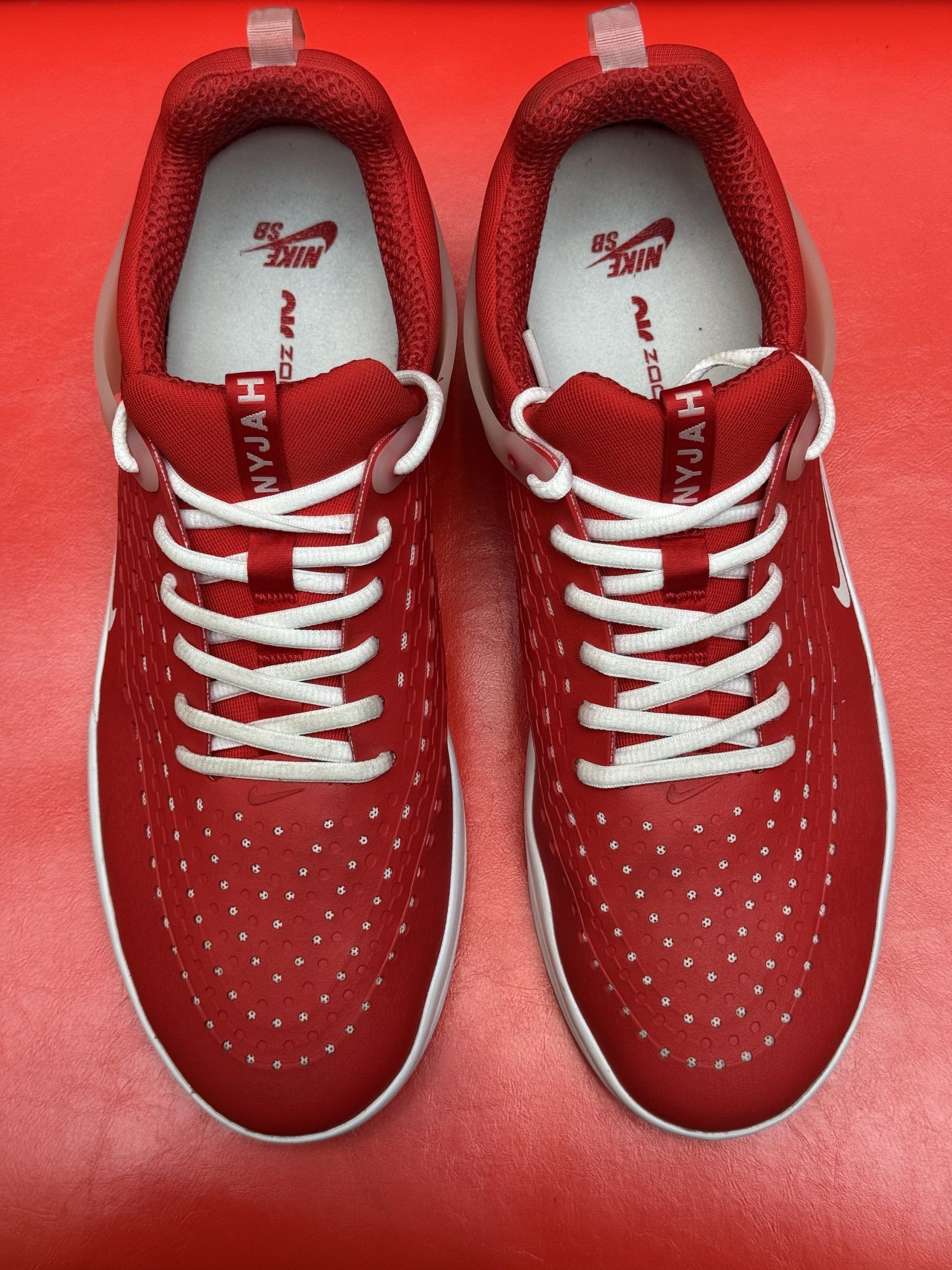 Red Nike shoes, one lying on its sole, against a red background. White sole, laces, and swoosh.