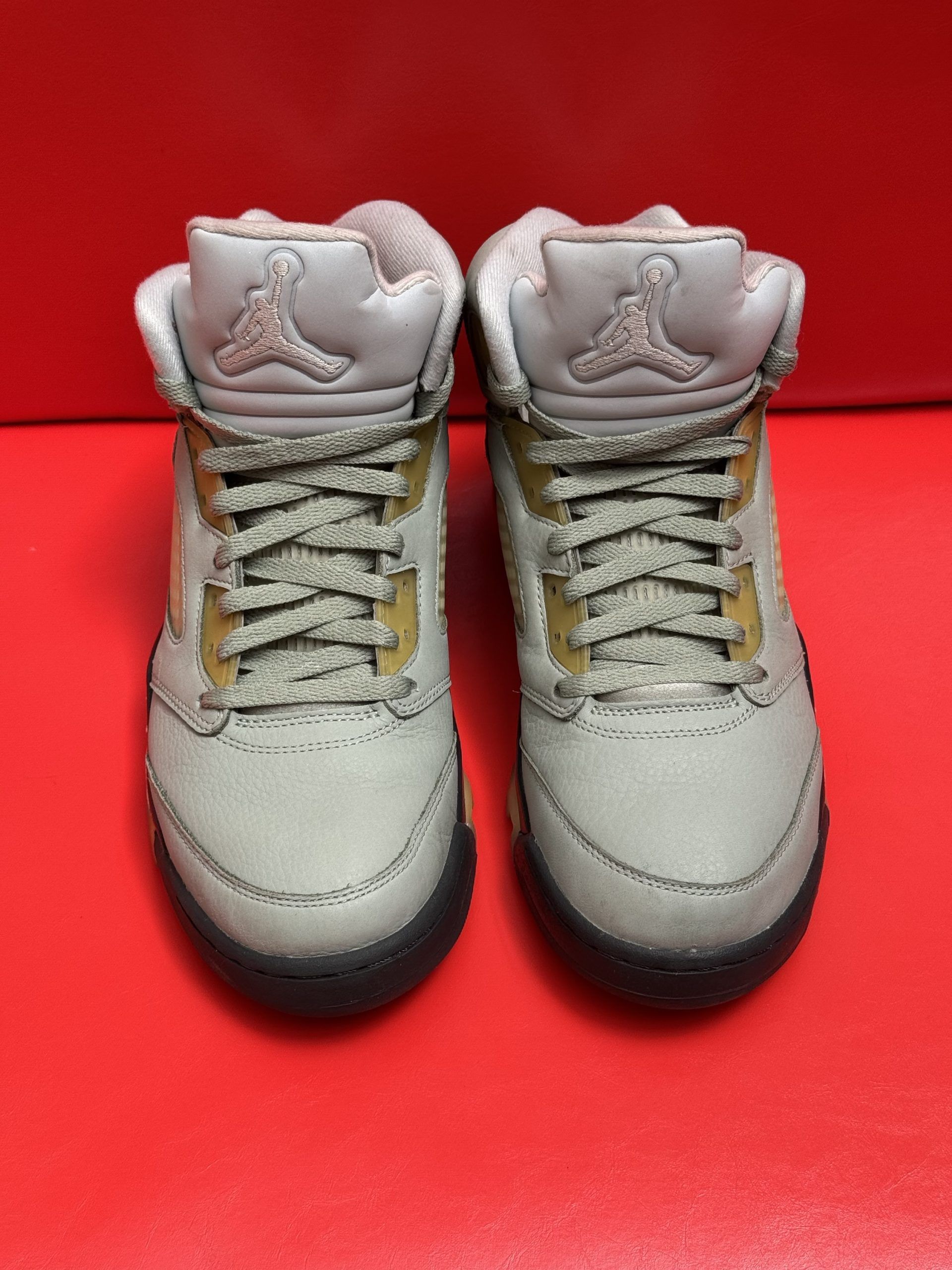 Gray, tan, and black Air Jordan 5 sneakers, one upside down showing the sole, on a red surface.