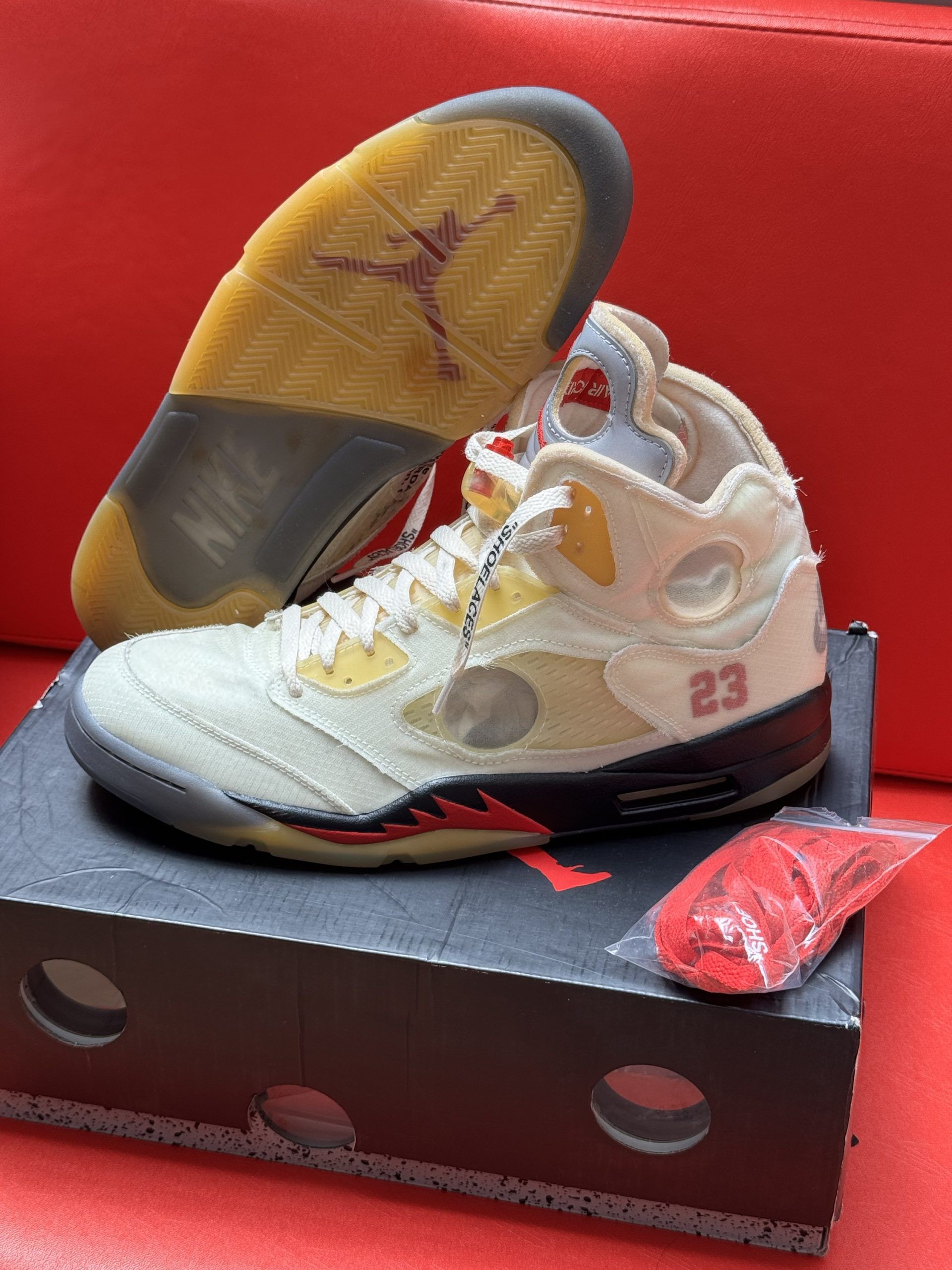 Off-White x Air Jordan 5 sneakers on a box. Off-white canvas with red accents, translucent sole, red laces.