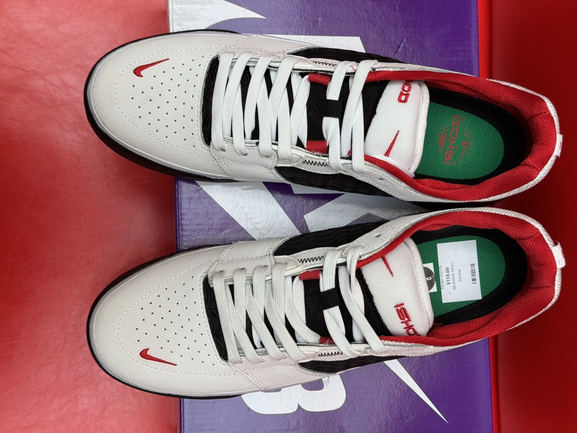White and red Nike SB sneakers on a purple box against a red backdrop, sole visible.