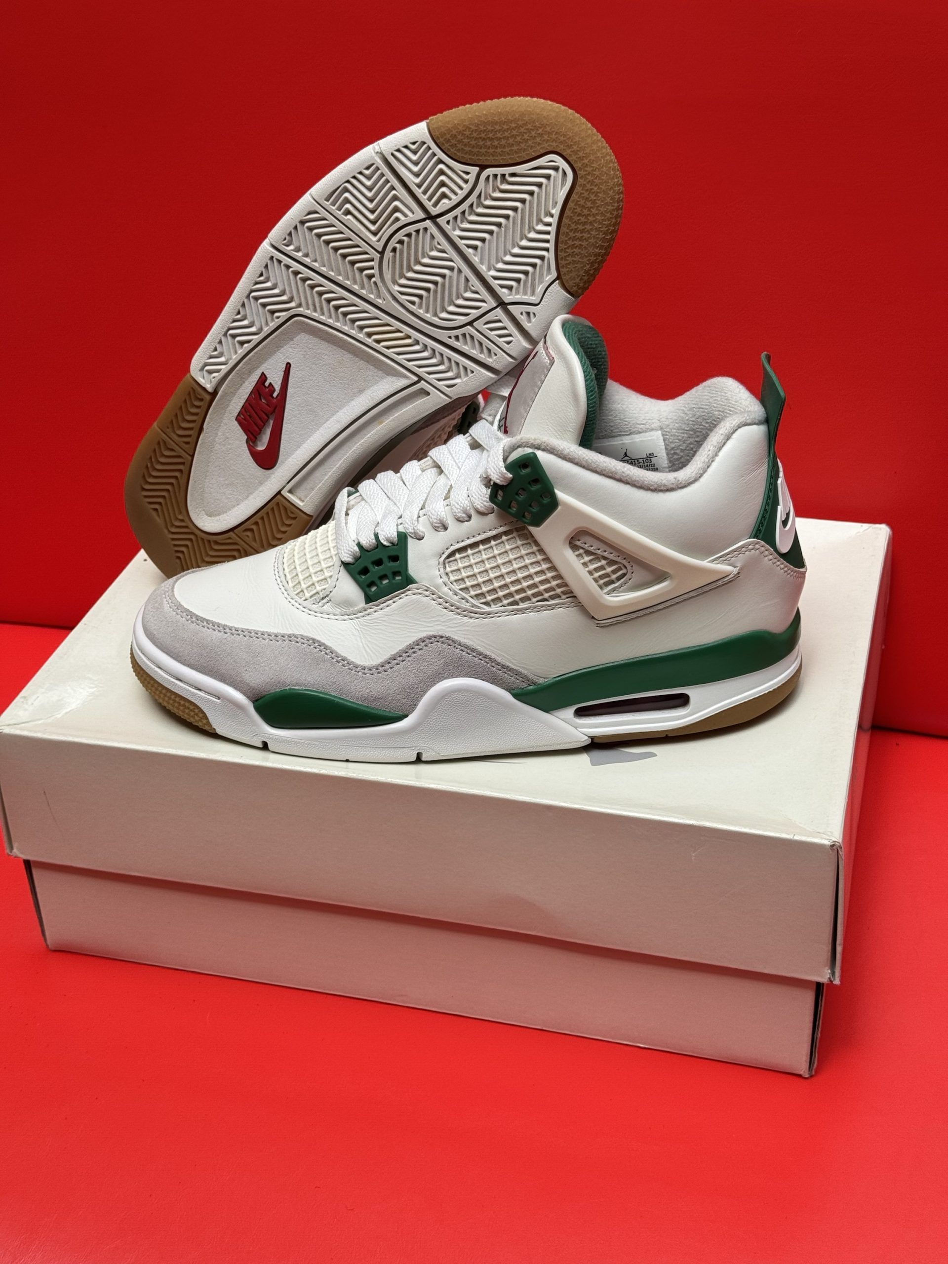 White and green Air Jordan 4 sneakers on a white box, one turned to show the sole. Red background.