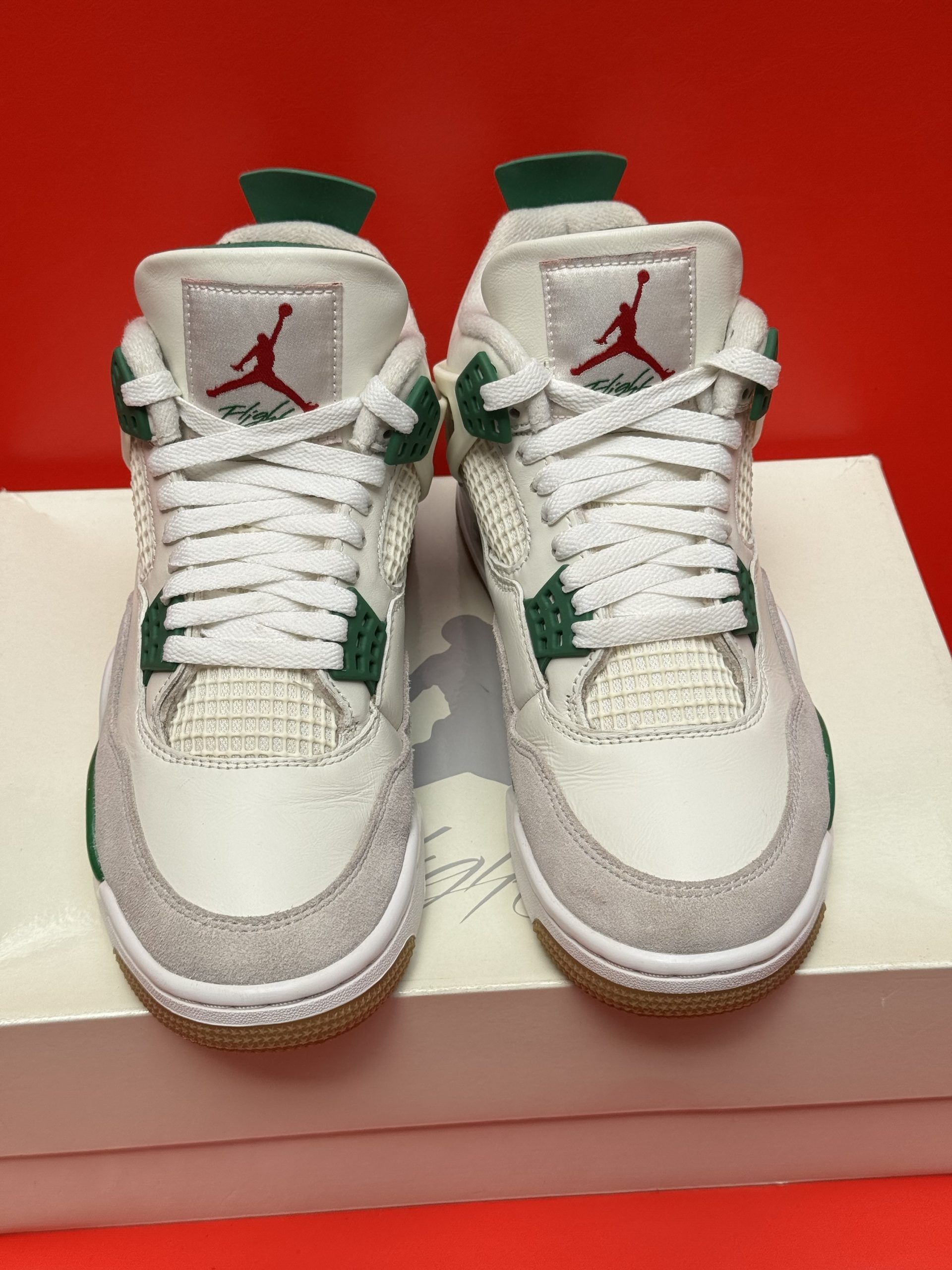 White and green Air Jordan 4 sneakers on a white box, one turned to show the sole. Red background.
