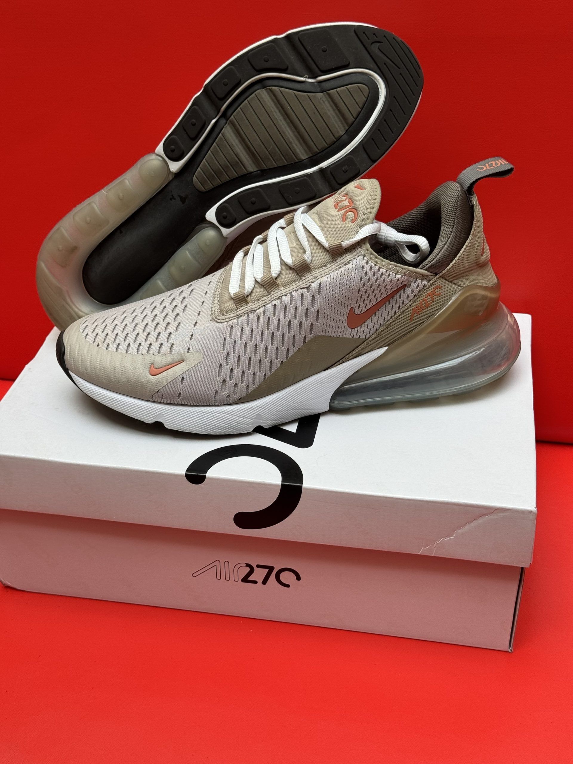 Beige and brown Nike Air Max 270 sneaker on top of a white box with the sole visible; red background.