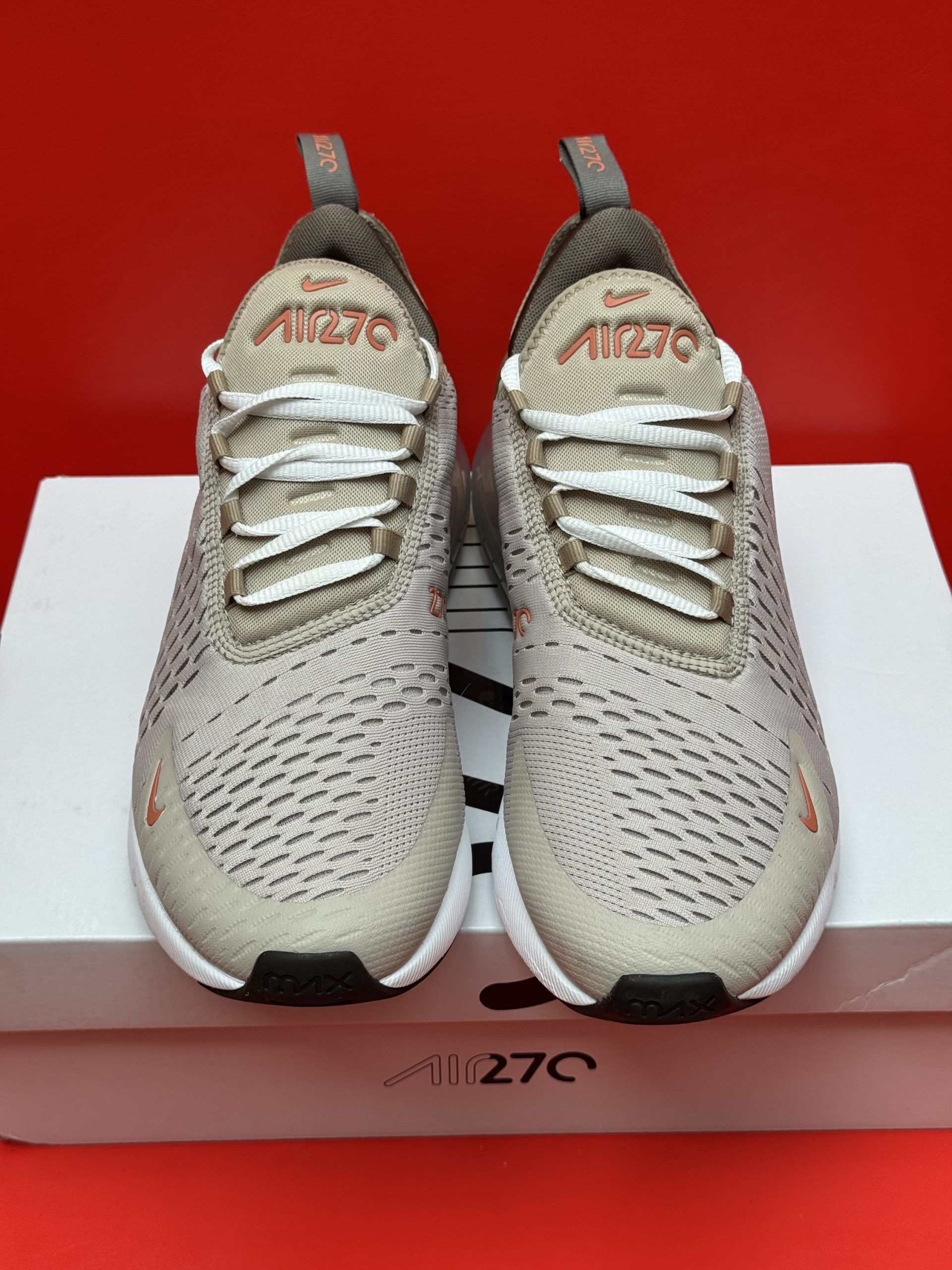 Beige and brown Nike Air Max 270 sneaker on top of a white box with the sole visible; red background.