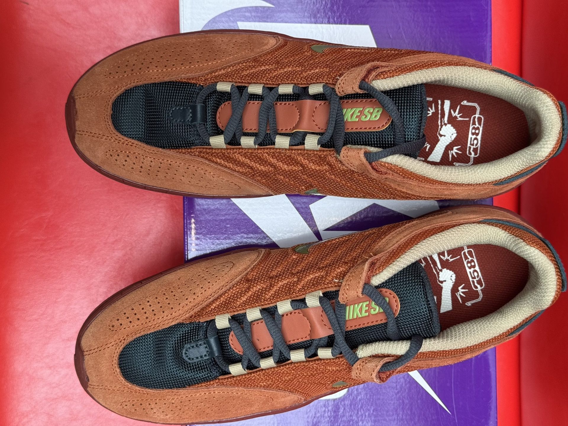 Nike SB Dunk Low Pro sneakers in orange and brown, on a purple SB box, with a red background.
