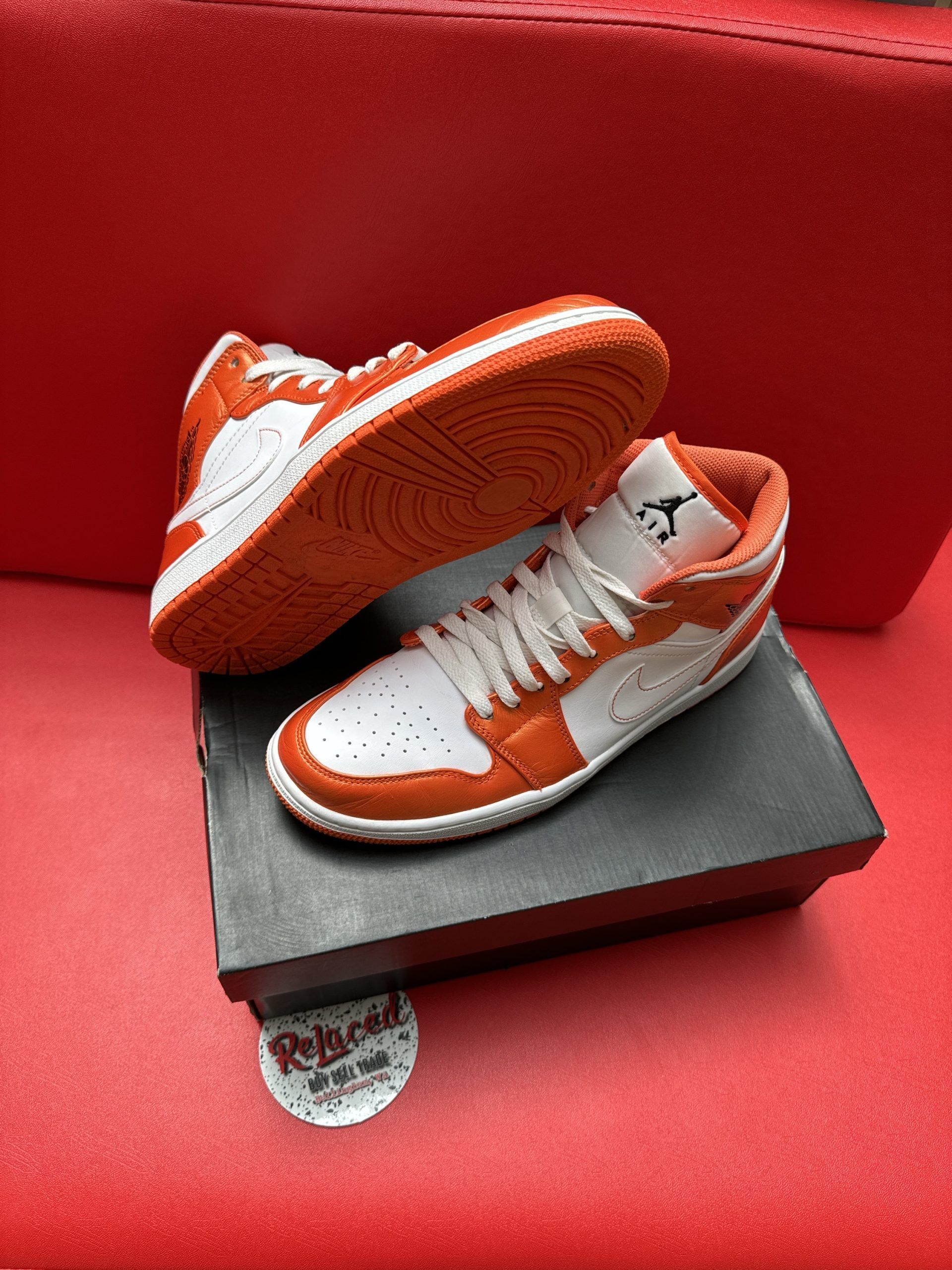 Orange and white Air Jordan sneakers on a black shoe box, set against a red background.