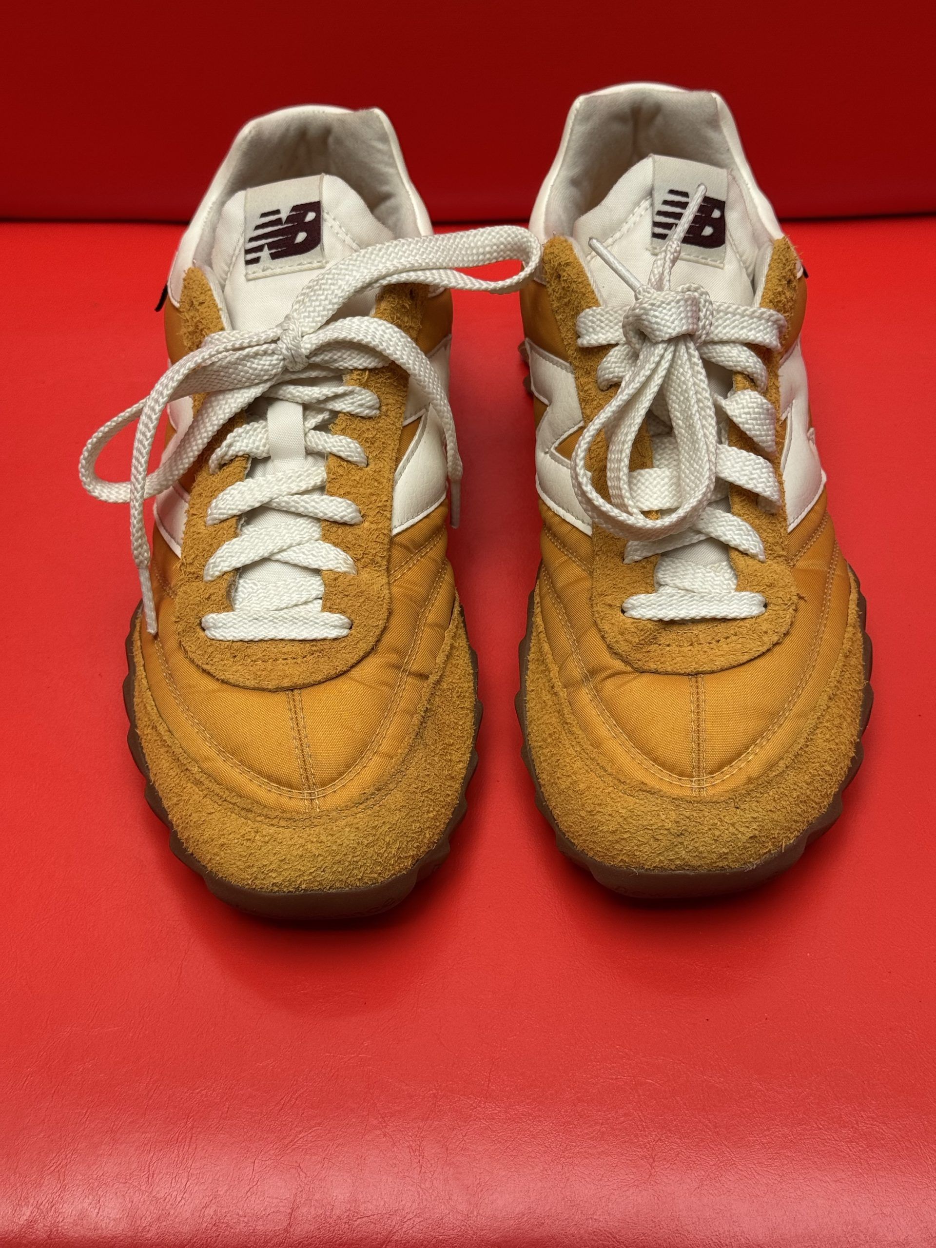 Yellow and white New Balance sneaker with brown sole on a red background.