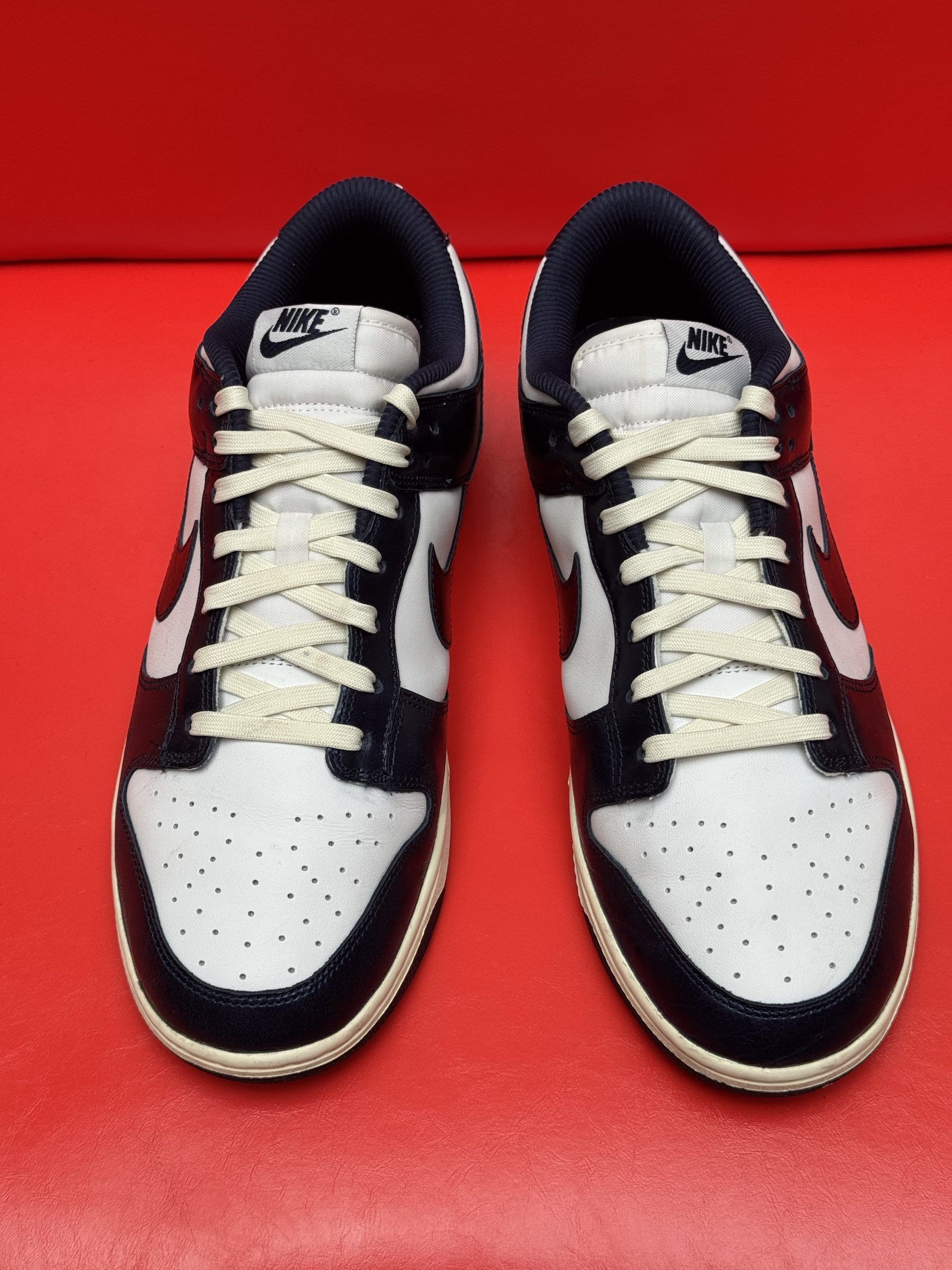 White and navy Nike Dunk Low sneakers, one showing sole, set against a red background.