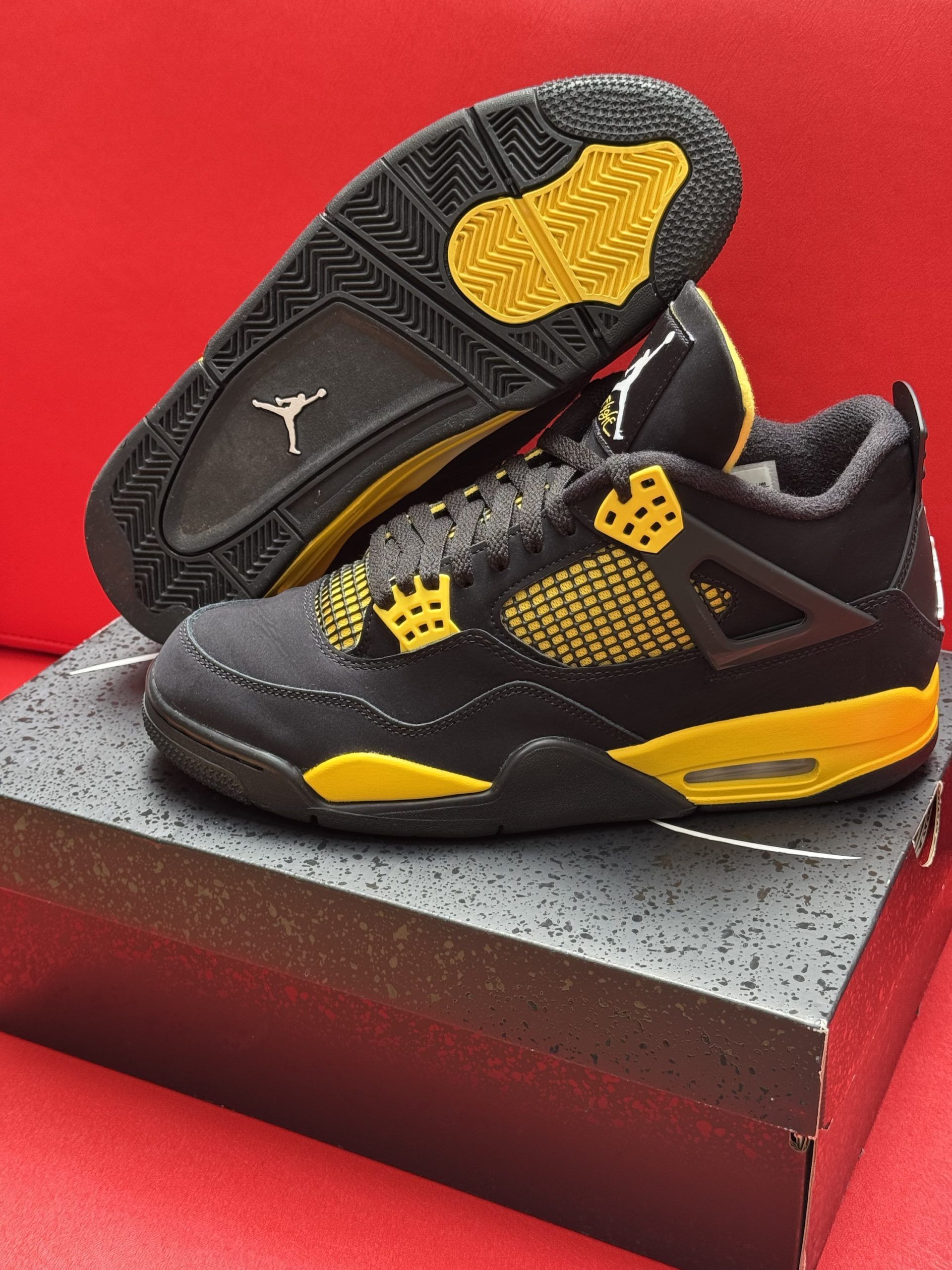 Black and yellow Air Jordan 4 sneakers on a box, sole visible.