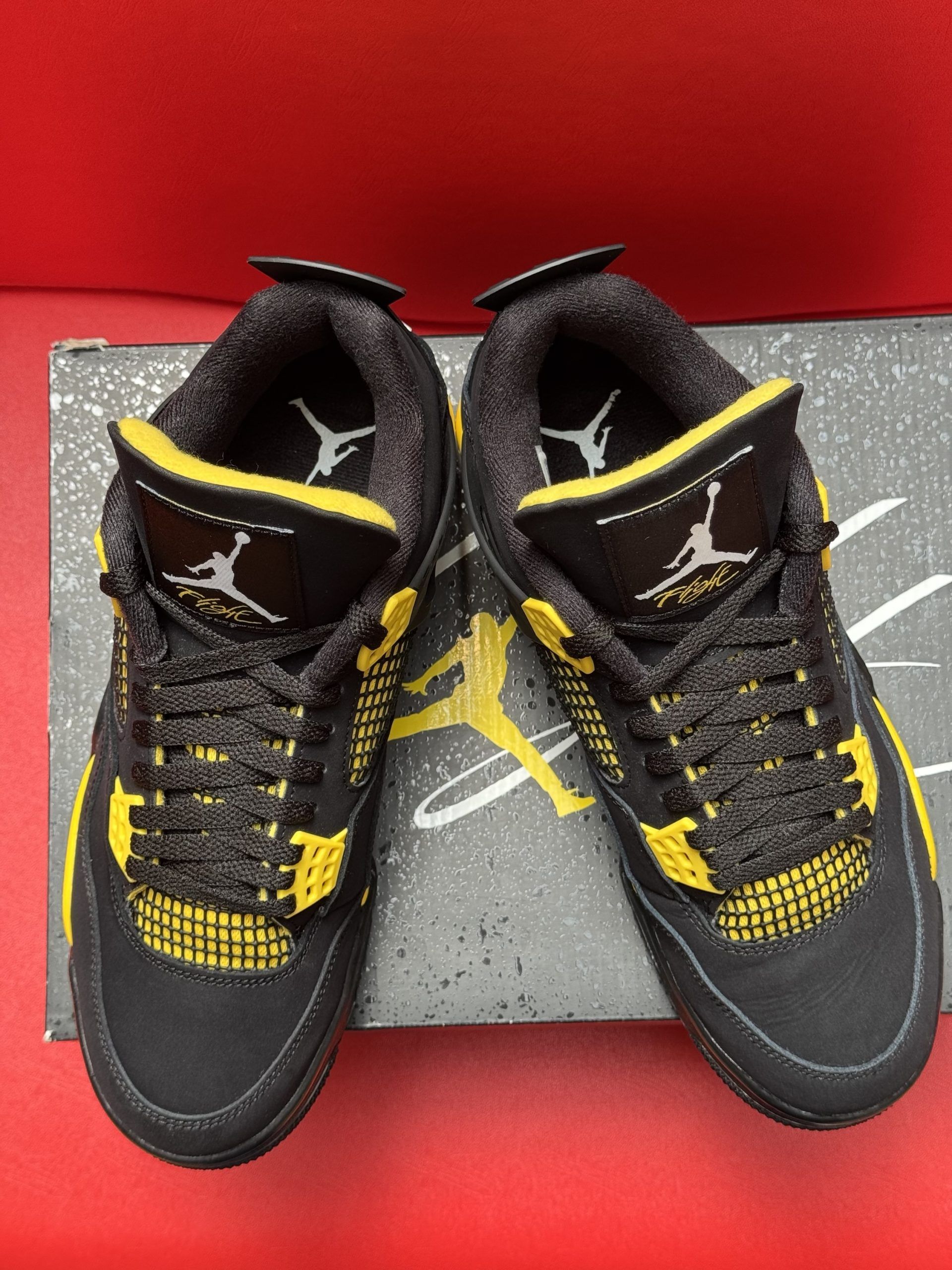 Black and yellow Air Jordan 4 sneakers on a box, sole visible.