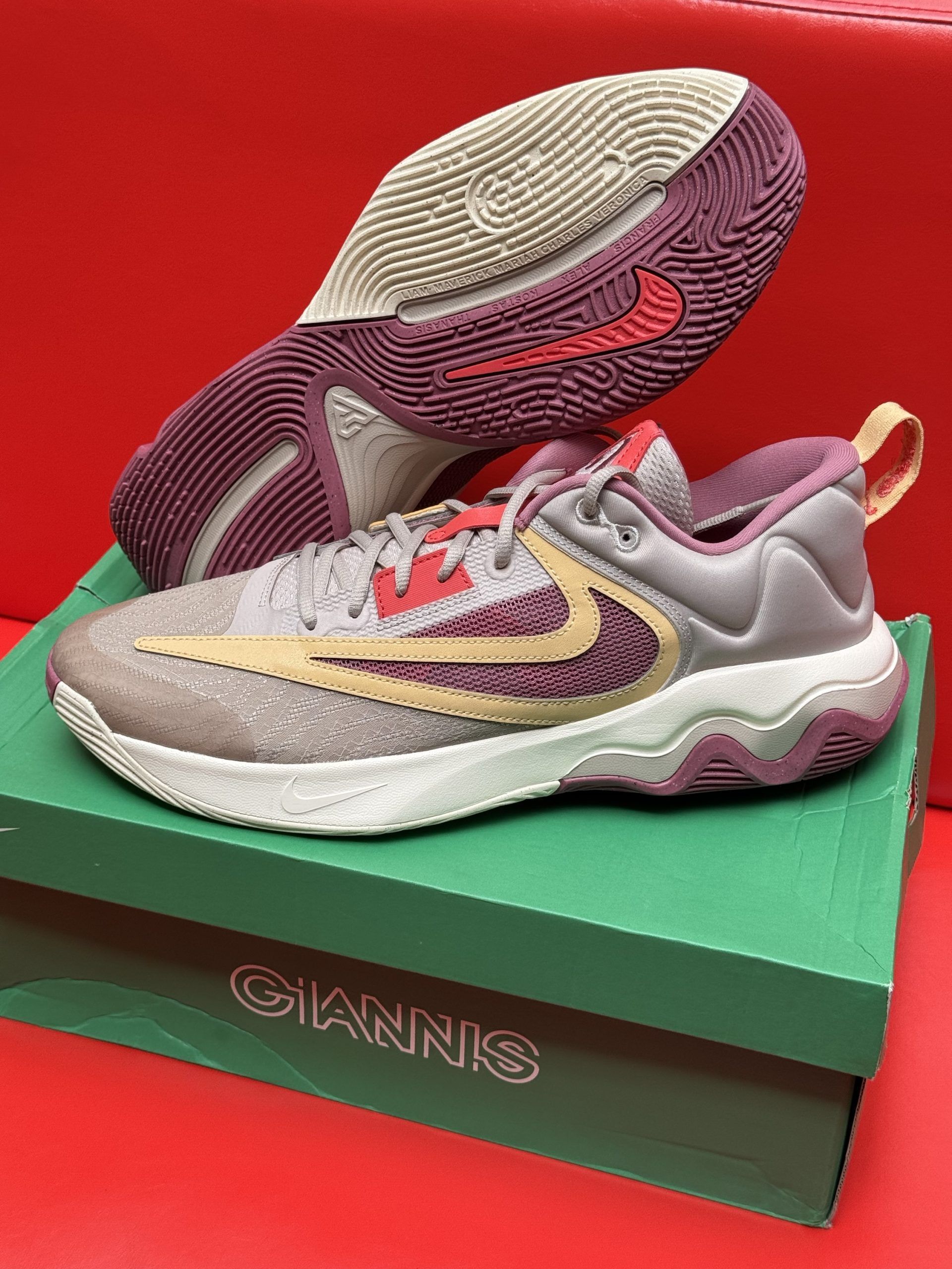 Nike Giannis Immortality 3 basketball shoe on a box. Gray and tan with red accents, maroon sole.