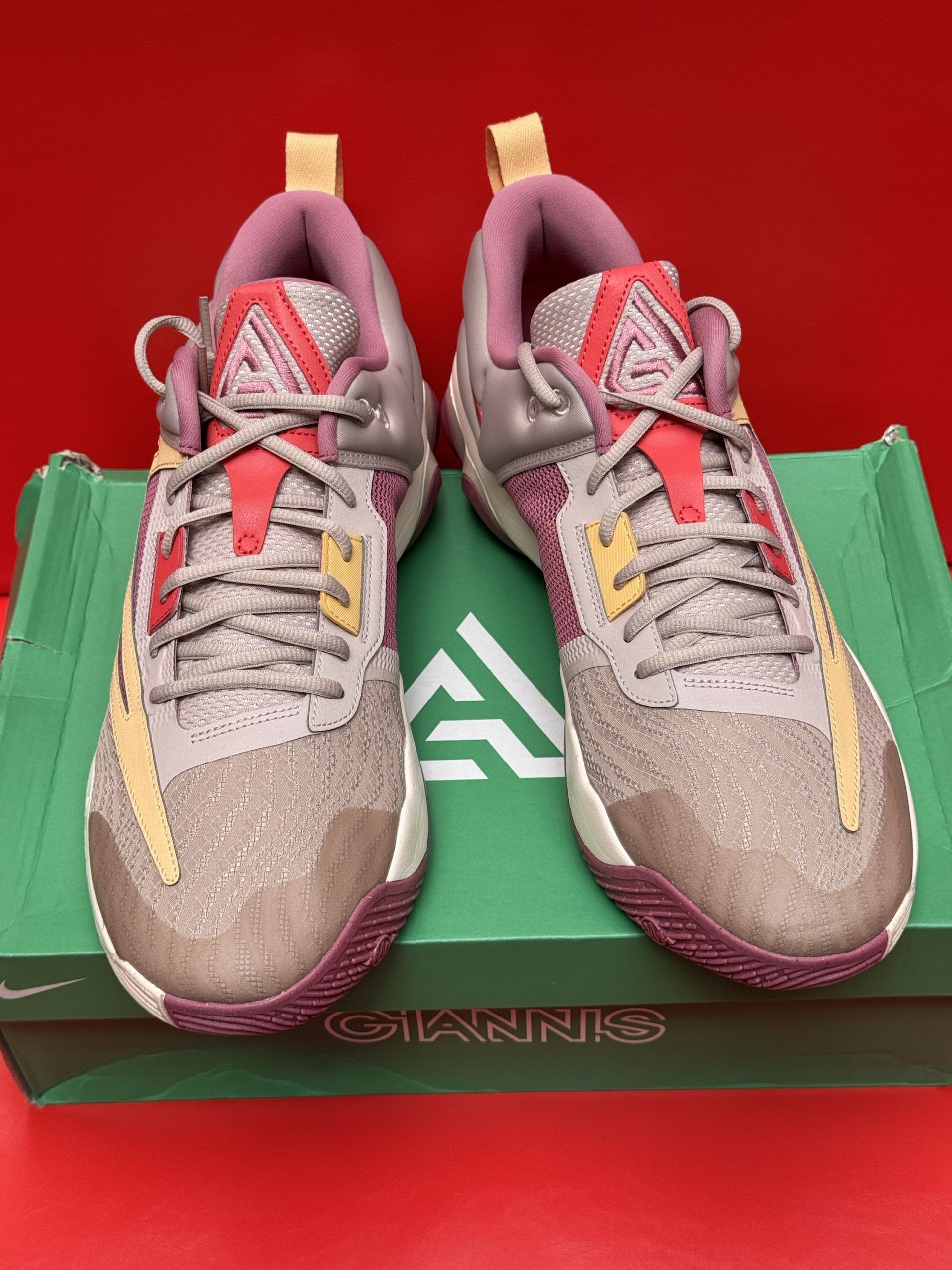 Nike Giannis Immortality 3 basketball shoe on a box. Gray and tan with red accents, maroon sole.