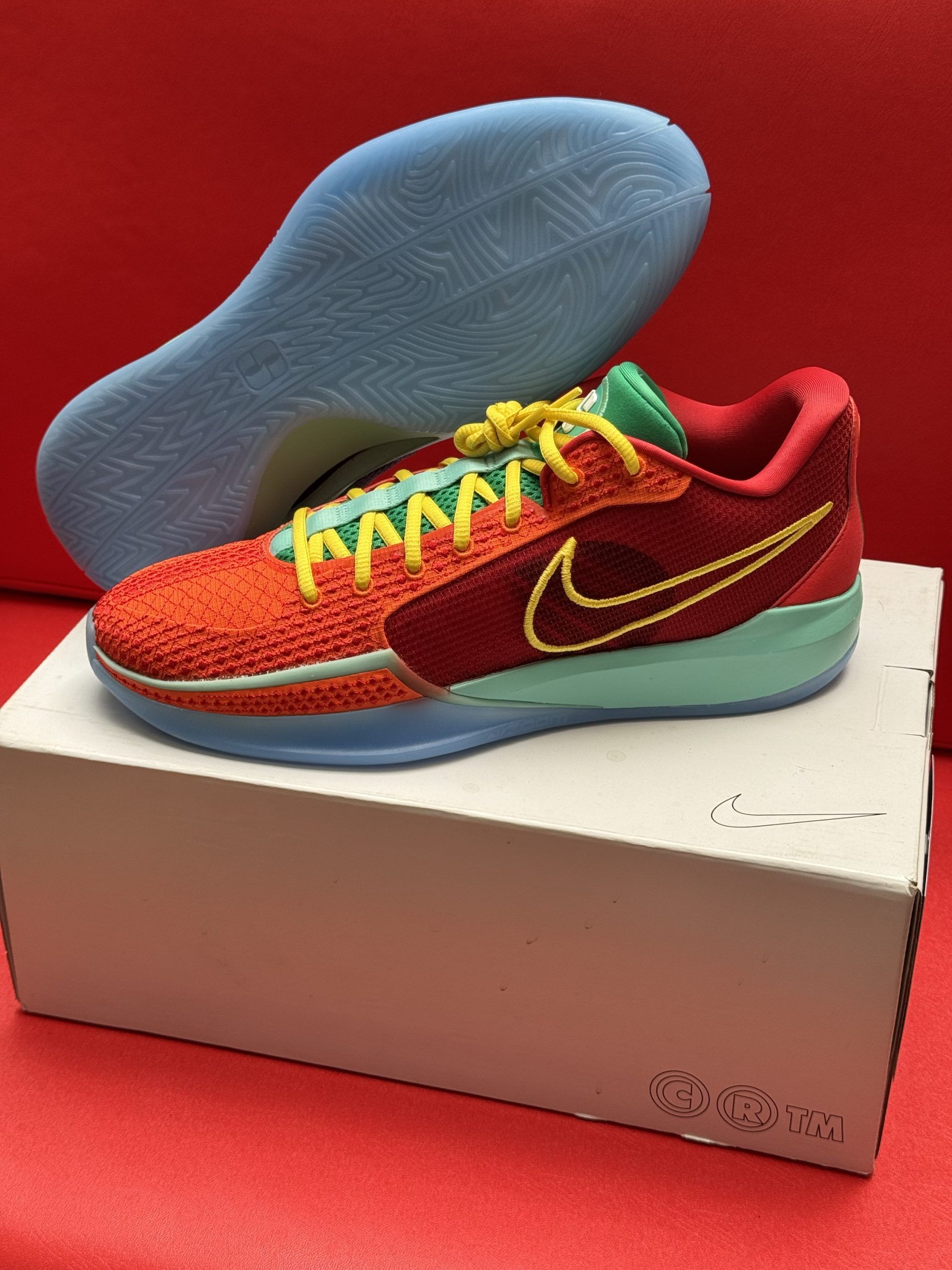 Red and yellow Nike sneaker on a box, with a light blue sole.