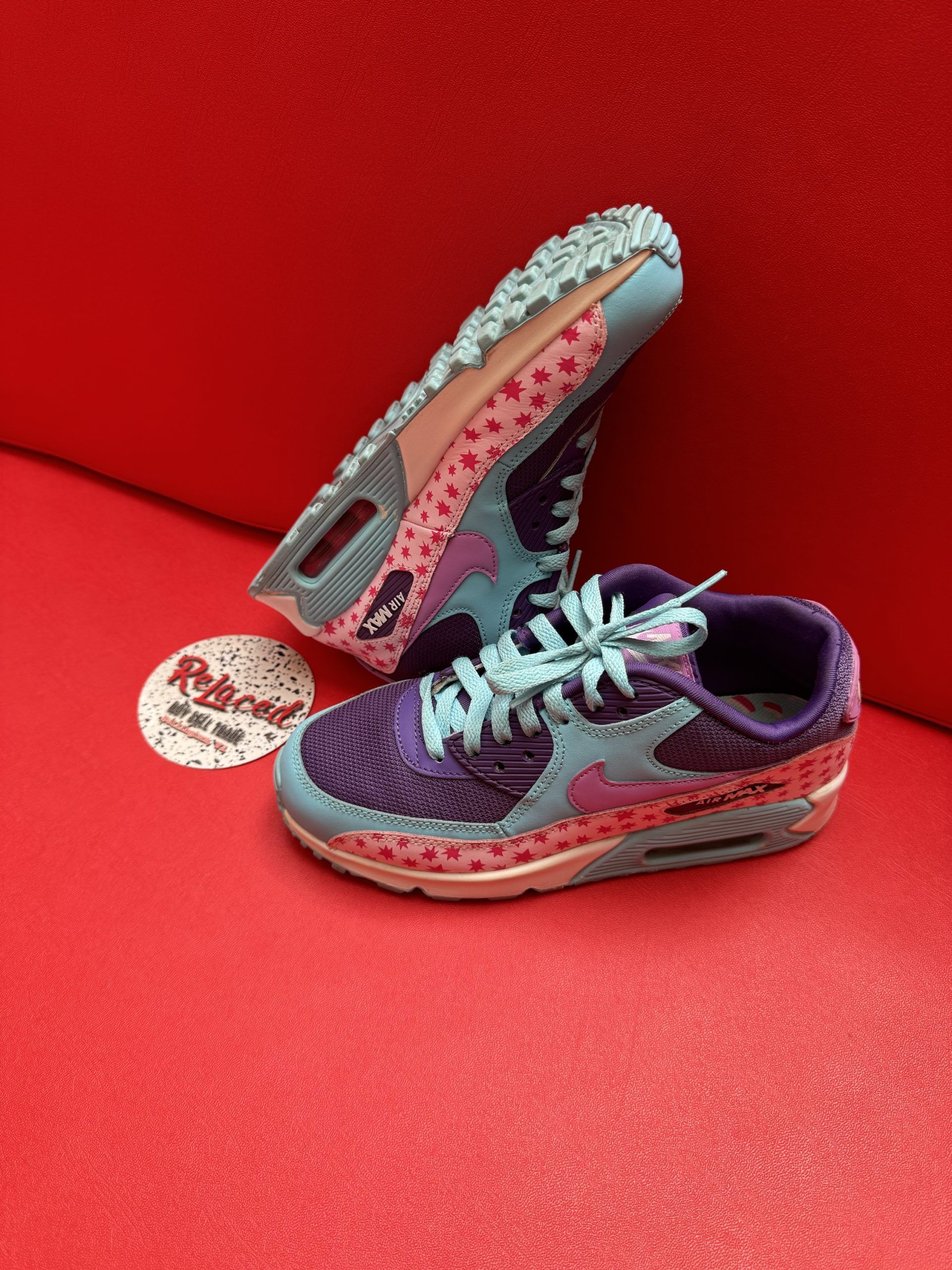Purple and blue Nike Air Max sneakers on a red surface, with a label nearby.