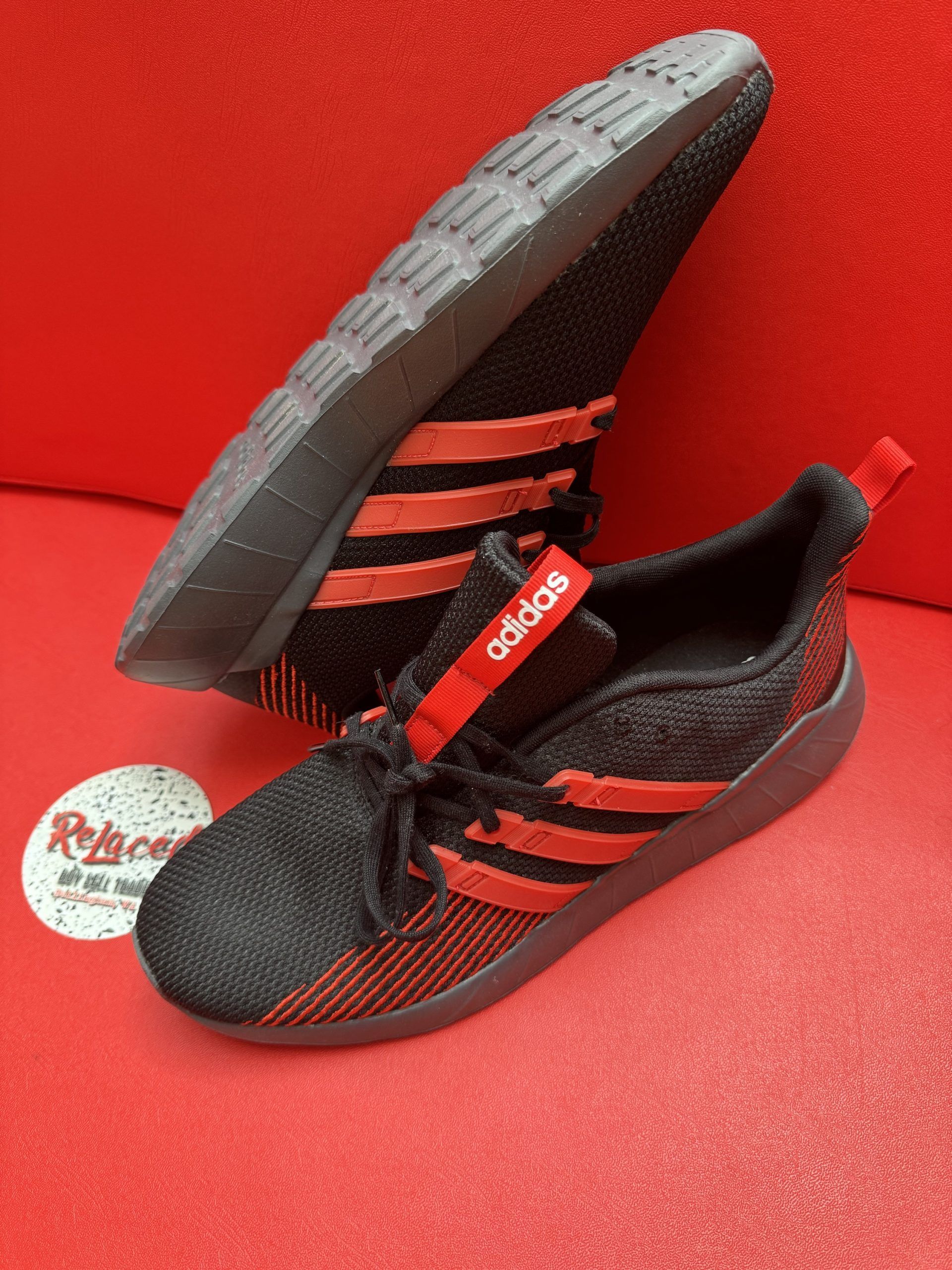 Black and red Adidas sneakers on a red surface; one shows the sole.