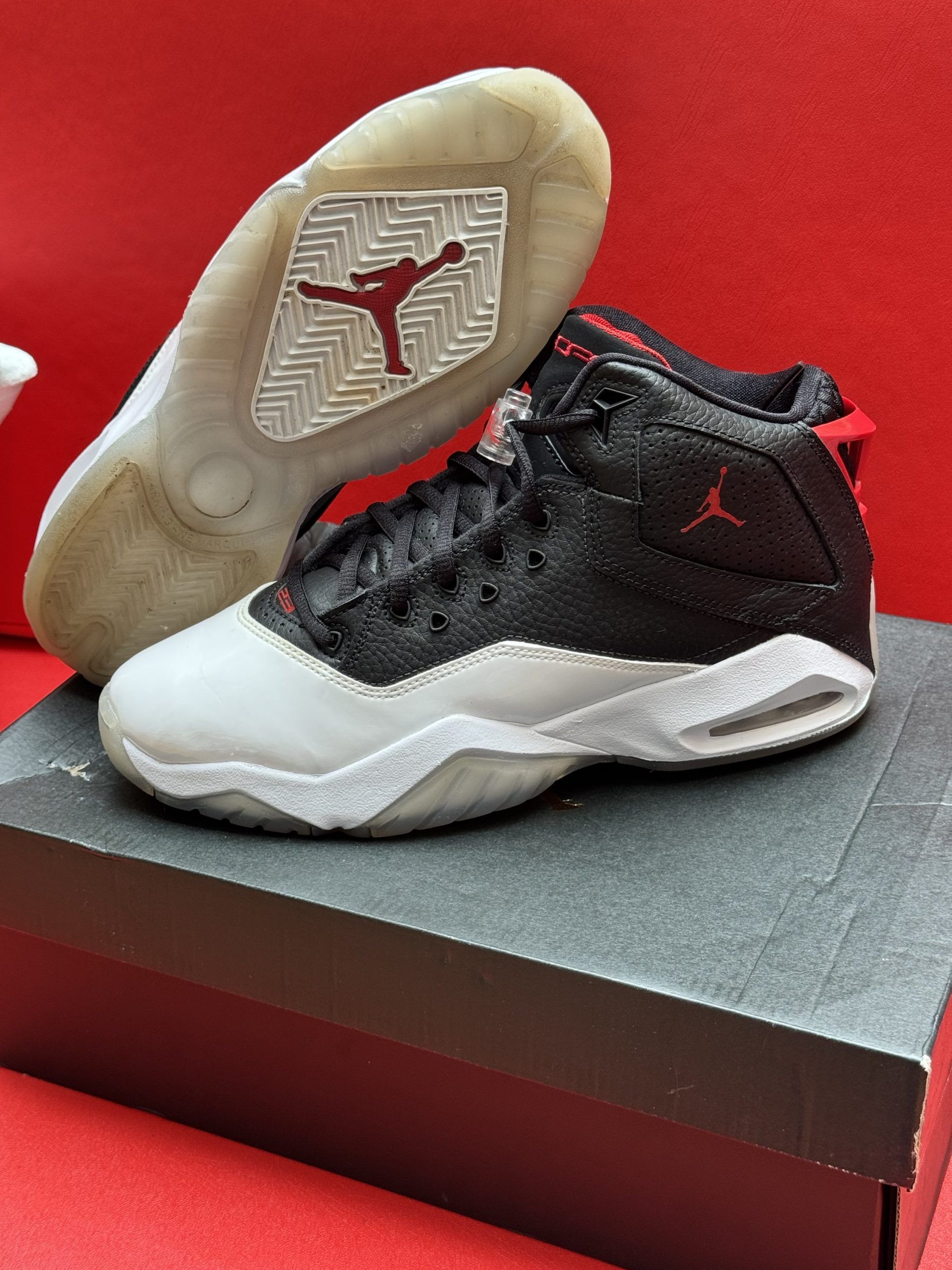Black and white Air Jordan sneakers with red accents, sitting on a shoebox. The sole has a red Jumpman logo.