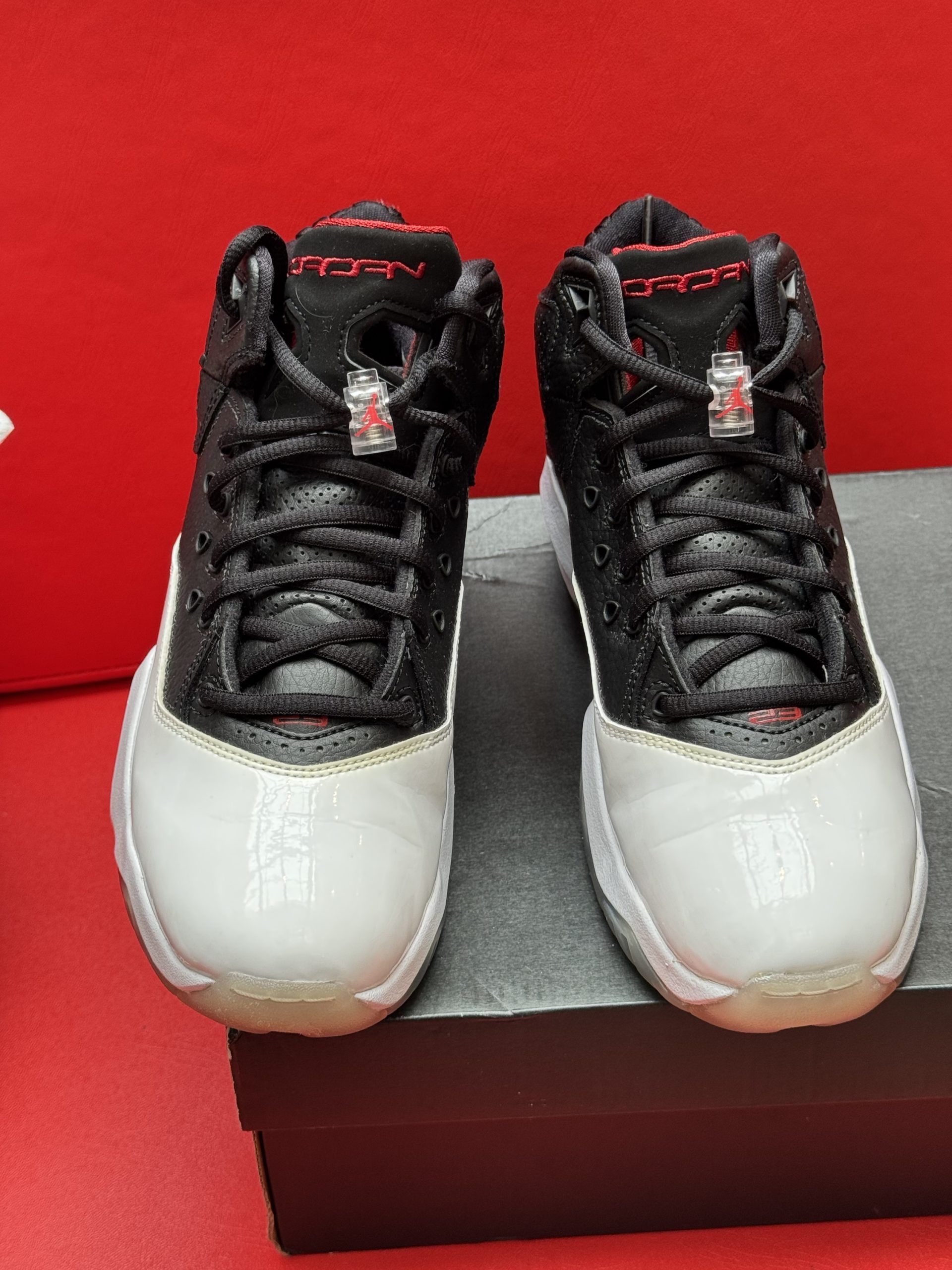 Black and white Air Jordan sneakers with red accents, sitting on a shoebox. The sole has a red Jumpman logo.