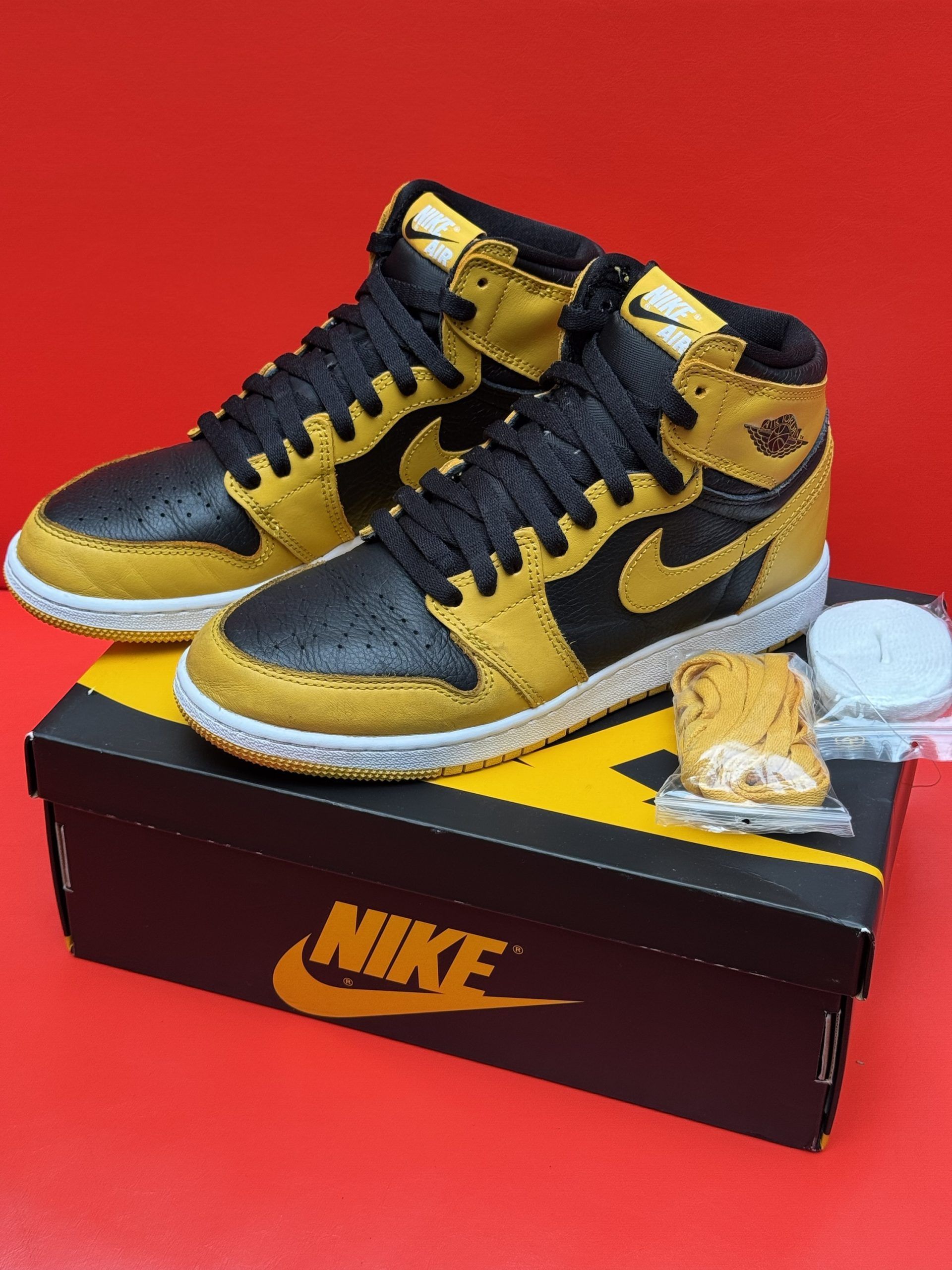 Black and gold Air Jordan 1 high-top sneakers with a yellow sole, presented on a Nike box.