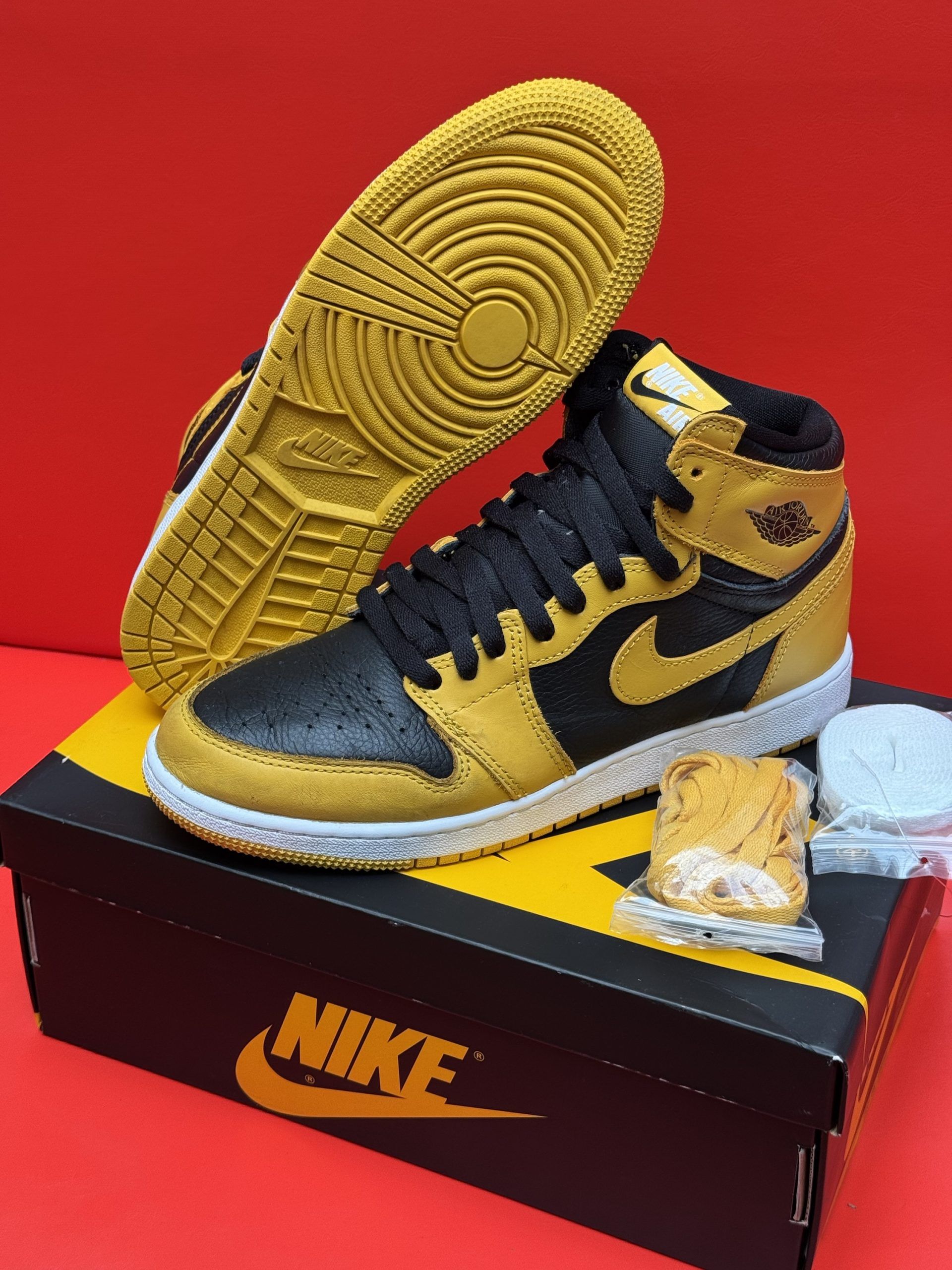 Black and gold Air Jordan 1 high-top sneakers with a yellow sole, presented on a Nike box.