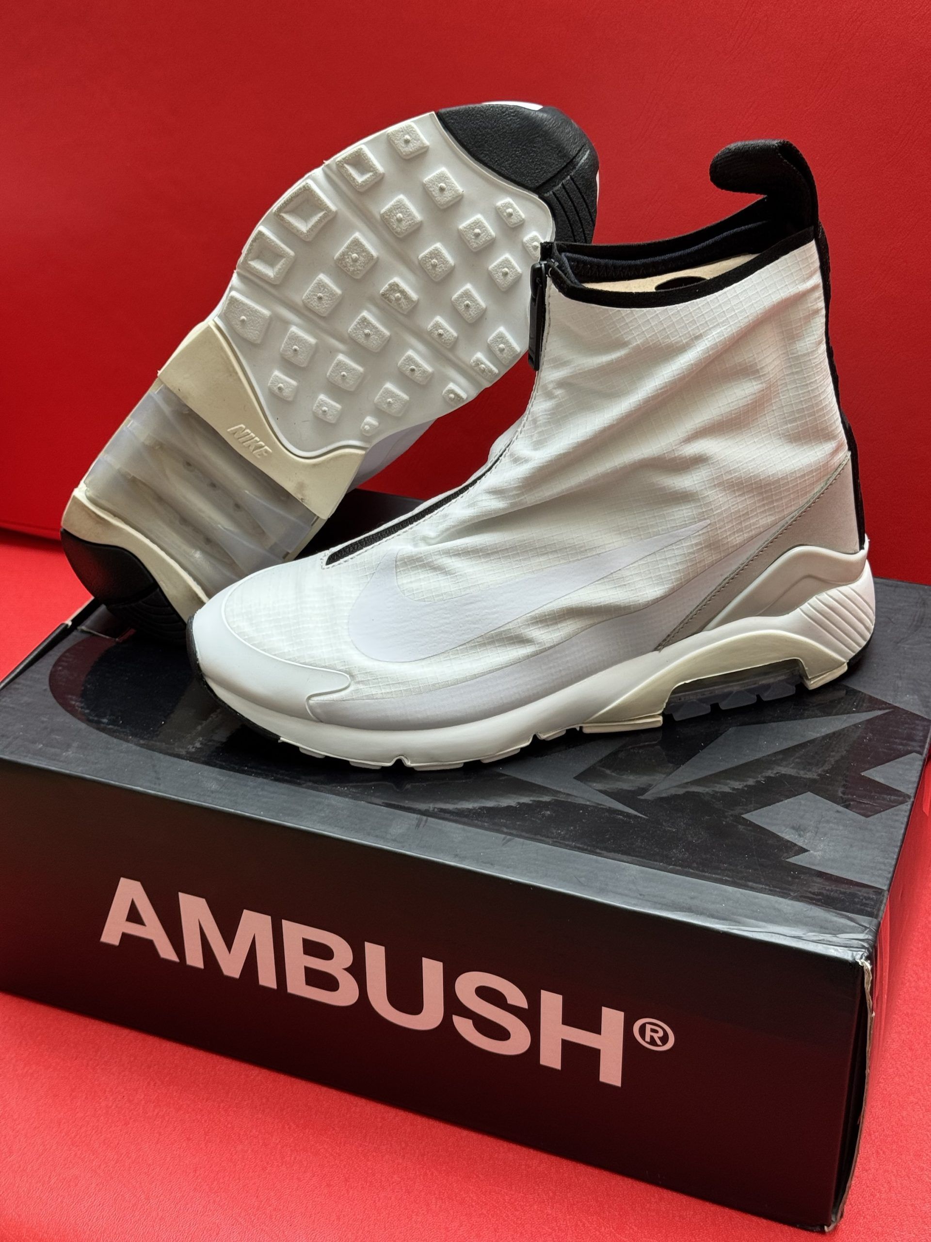 White Nike Ambush sneakers on a black box with the brand name.