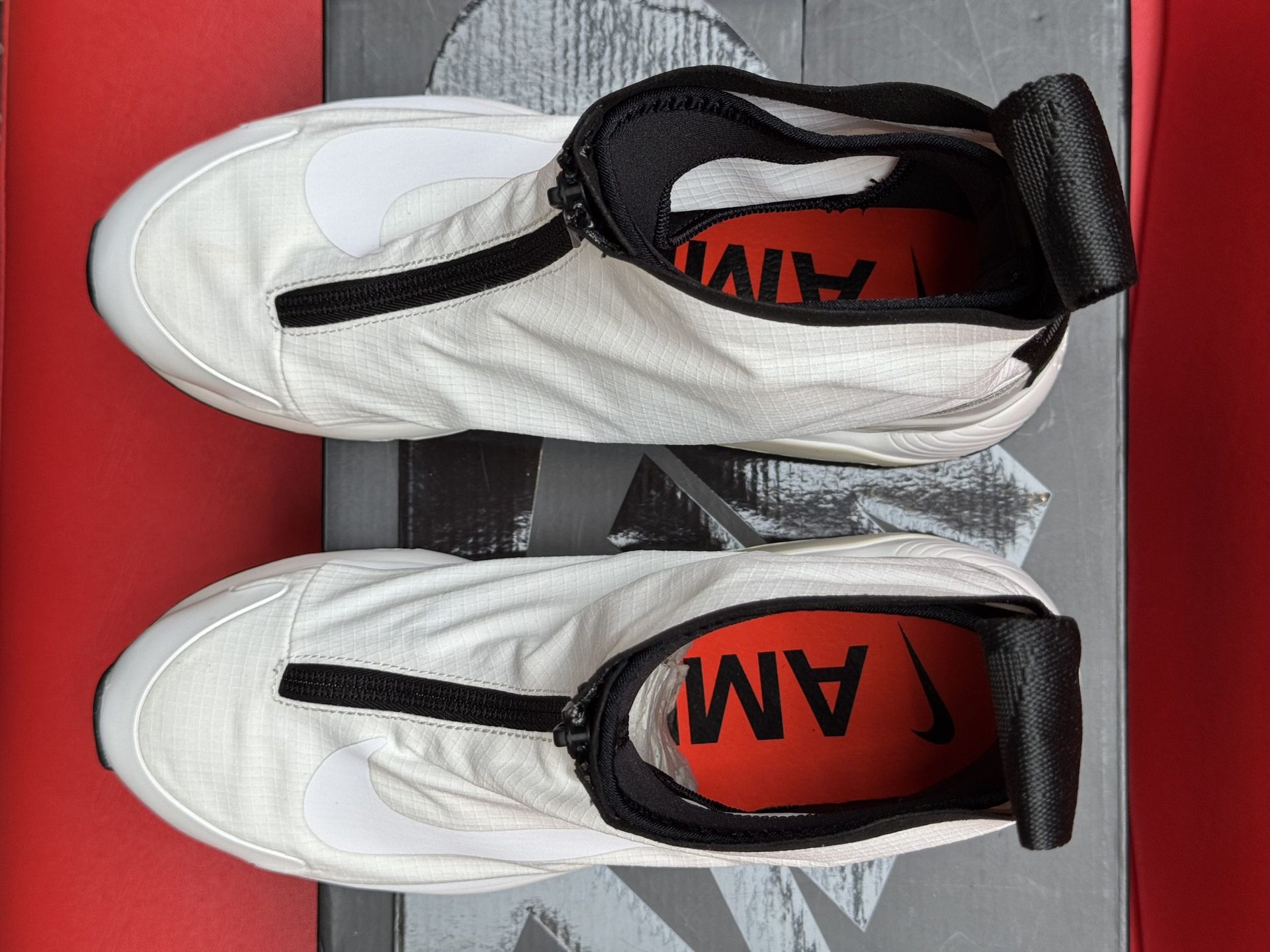 White Nike Ambush sneakers on a black box with the brand name.