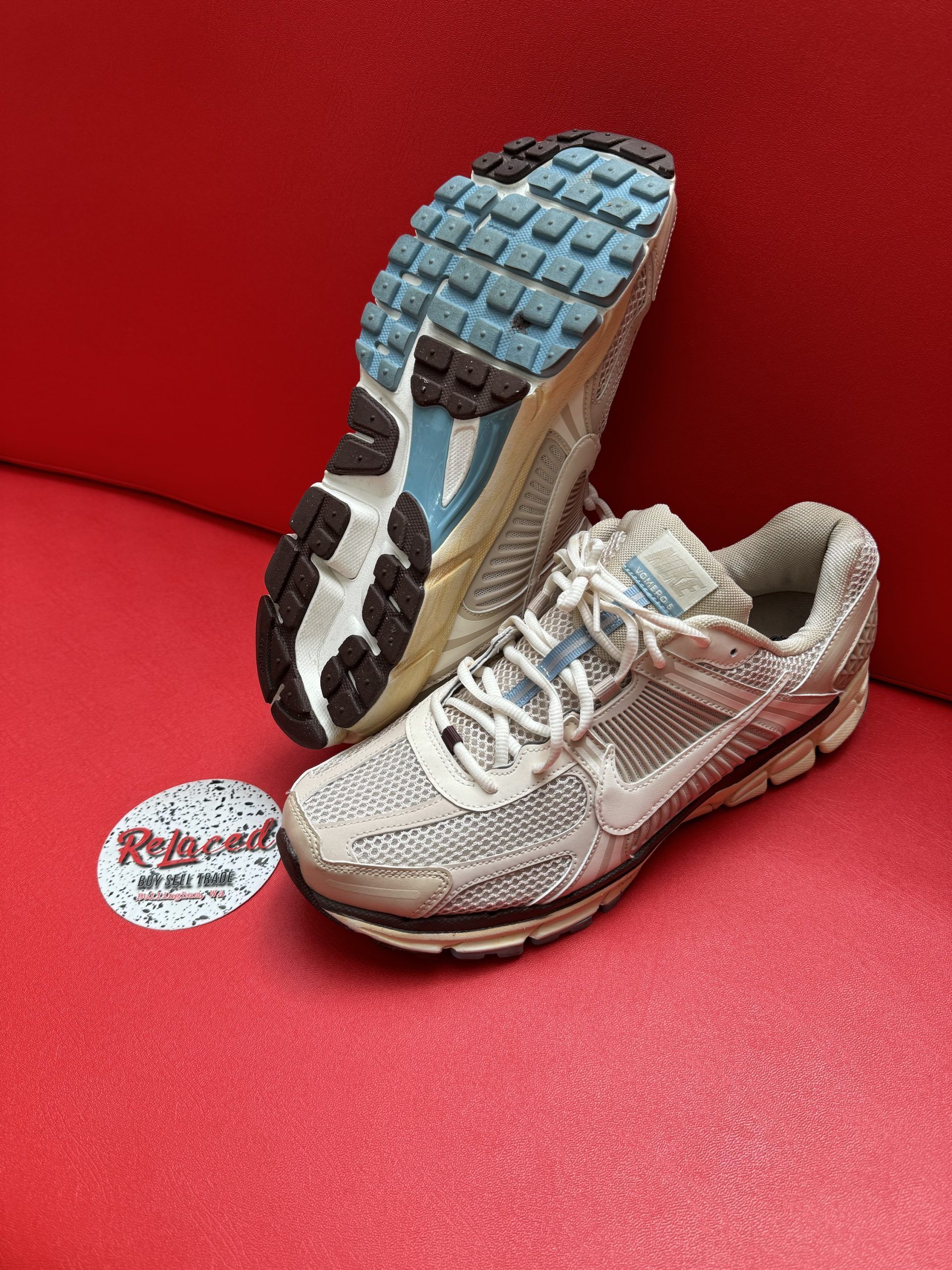 Pair of worn Nike sneakers on a red surface, one upside down showing the blue sole.