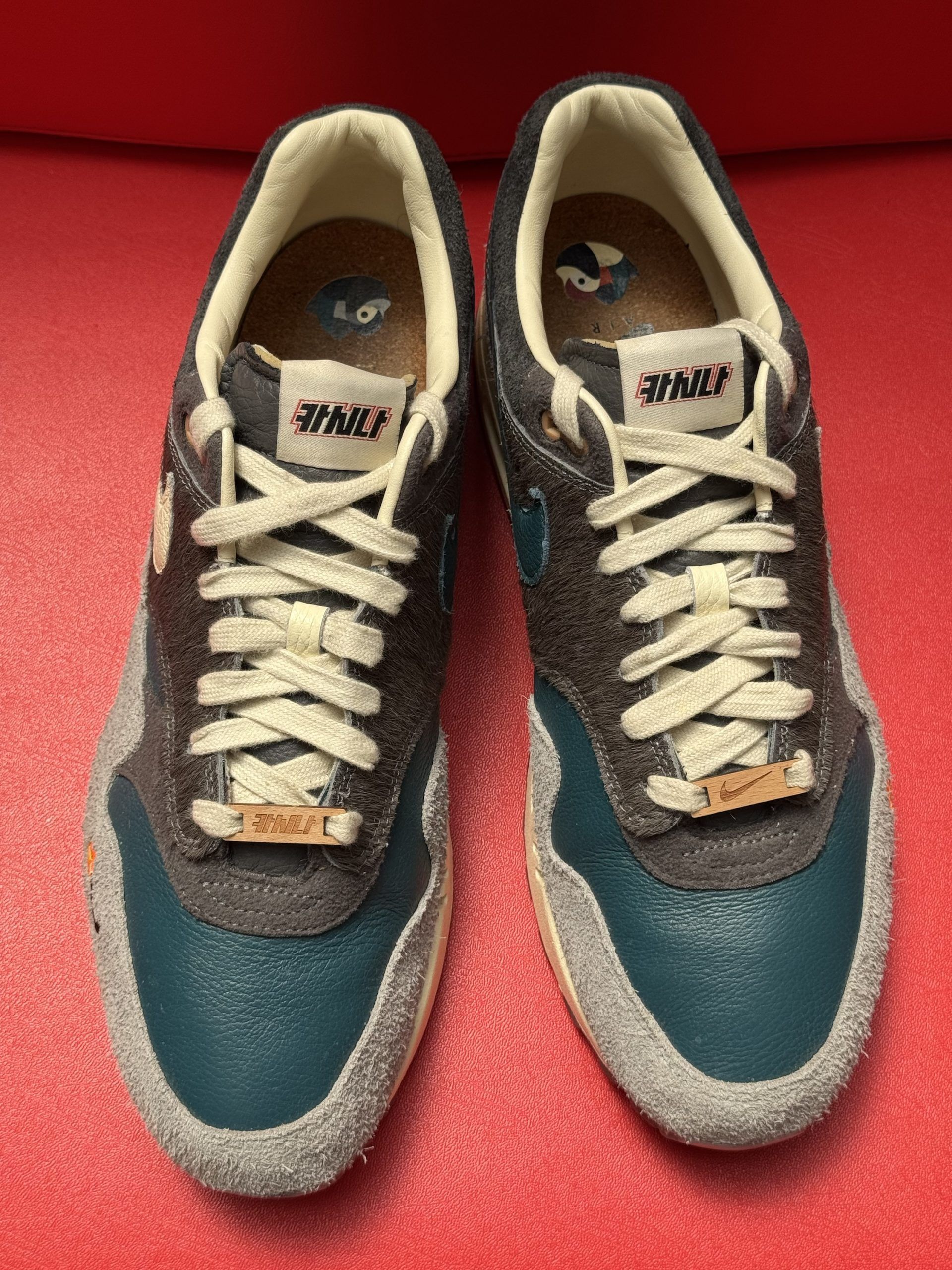 Nike Air Max 1 sneaker with a blue, gray, and cream color scheme, with a clear sole on a red surface.