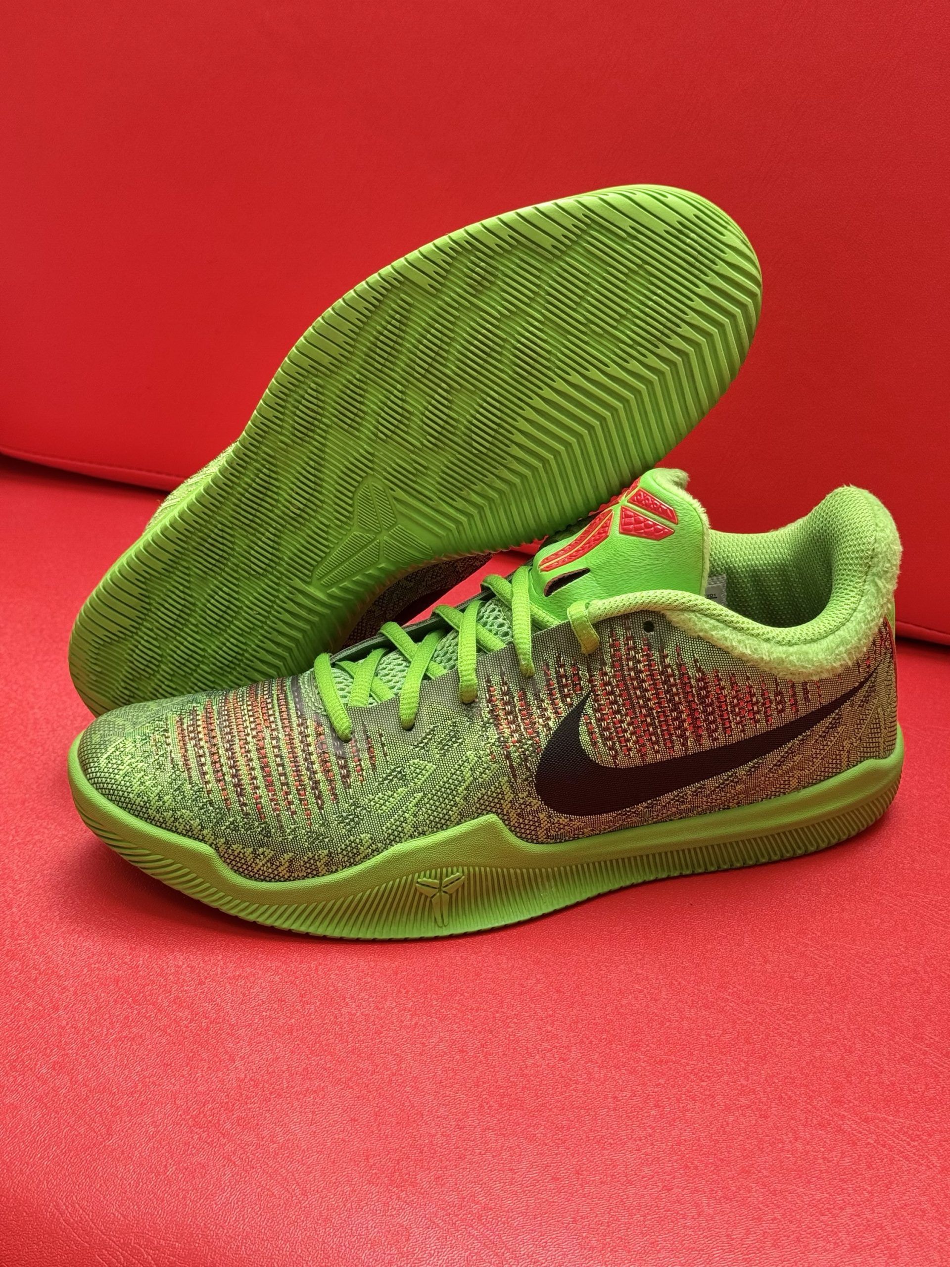 Green and brown Nike Kobe 11 basketball shoes on a red surface.