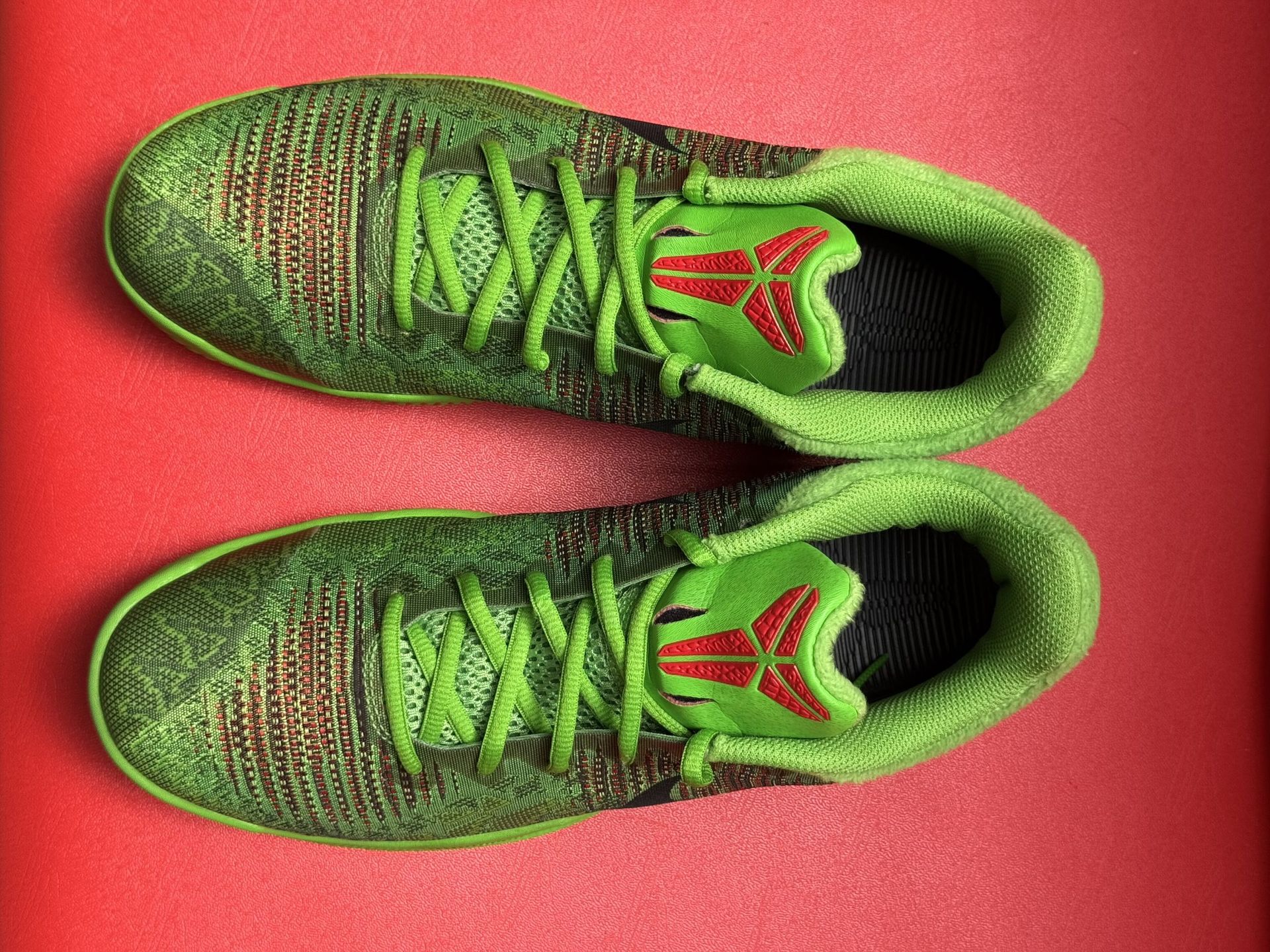 Green and brown Nike Kobe 11 basketball shoes on a red surface.