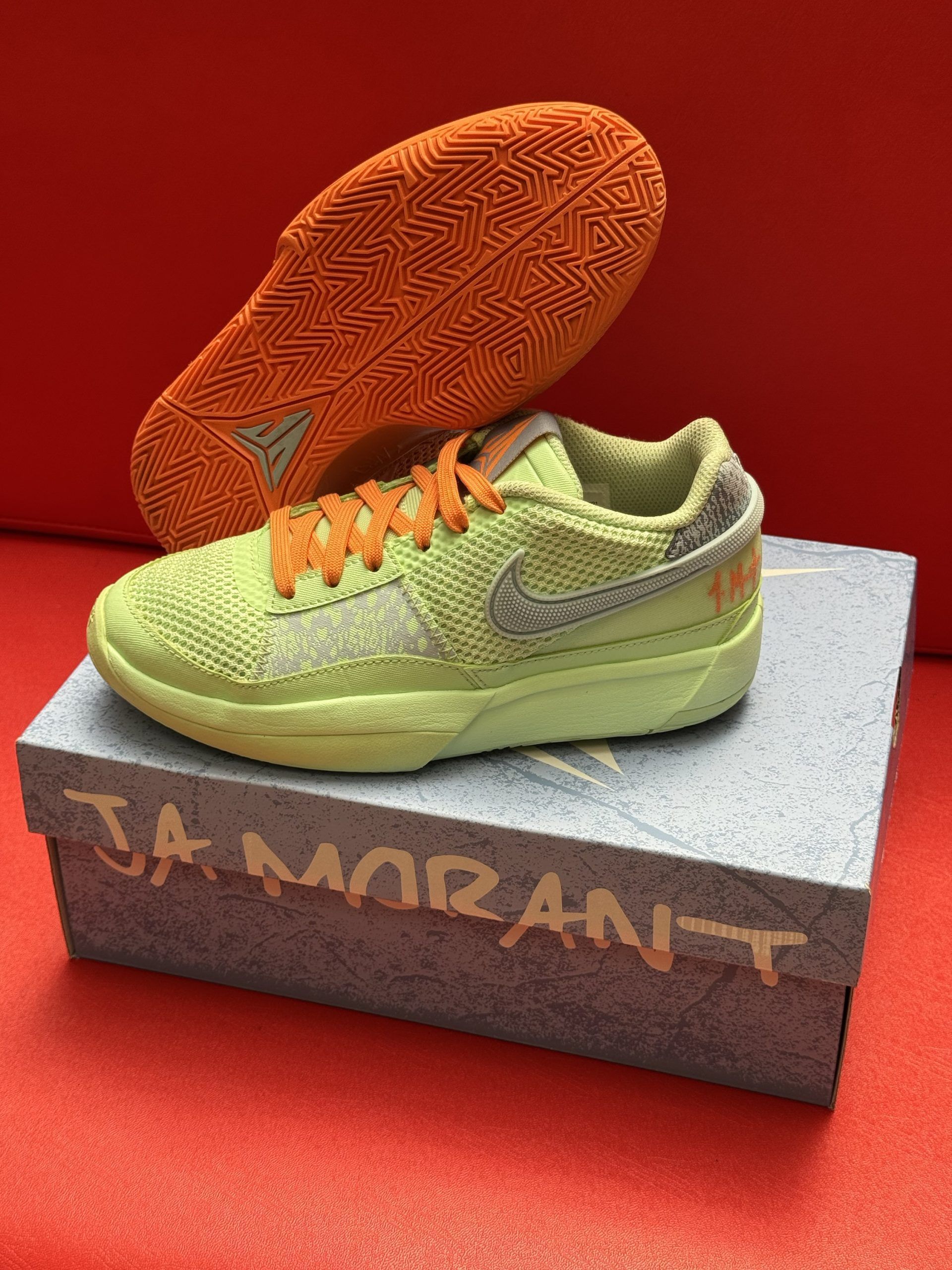 Lime green Ja Morant Nike basketball sneaker on gray box with orange sole.
