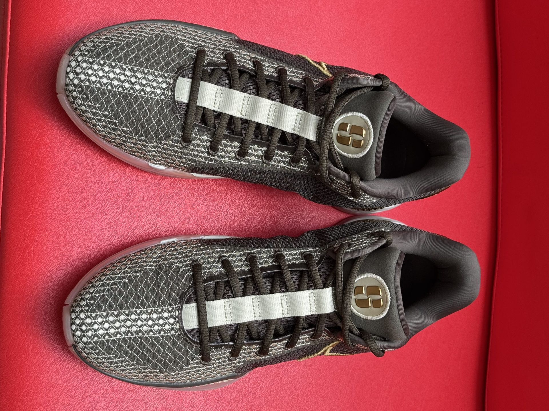 Pair of black and gold Nike Kobe basketball sneakers on a red surface, with text on the translucent soles.