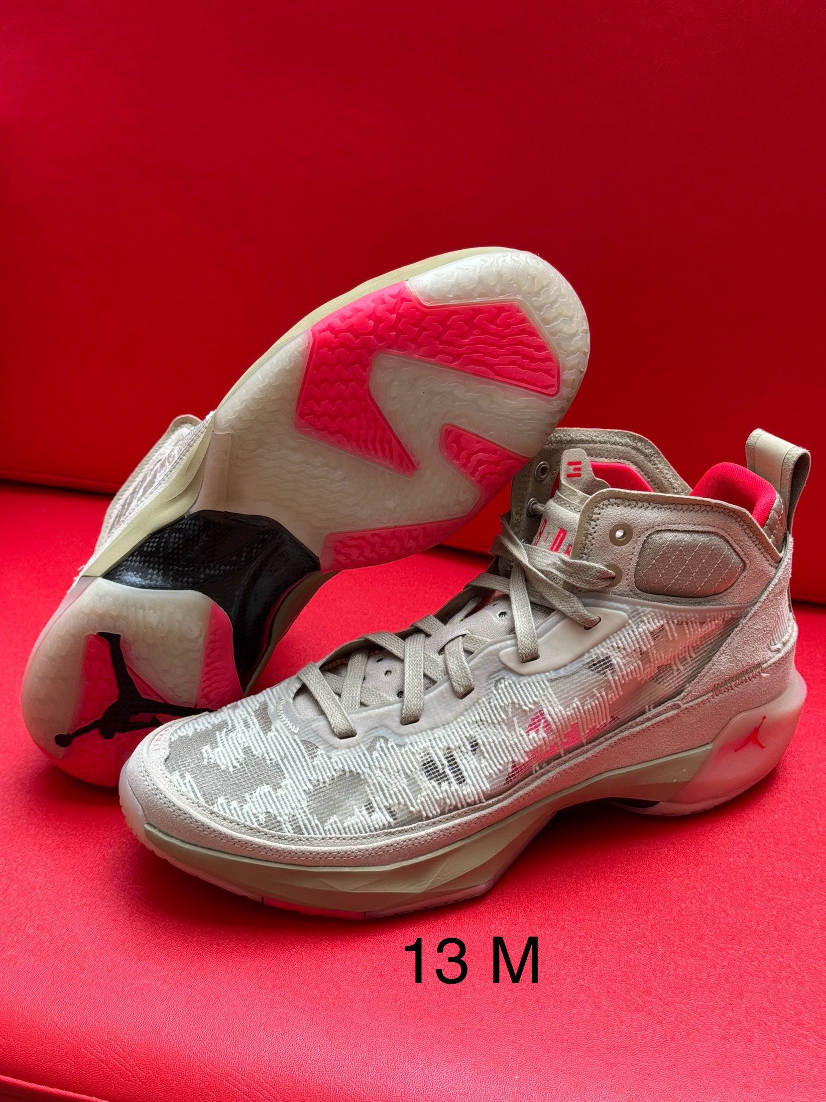 Tan and white Jordan basketball shoes with pink accents on a red surface. Marked 