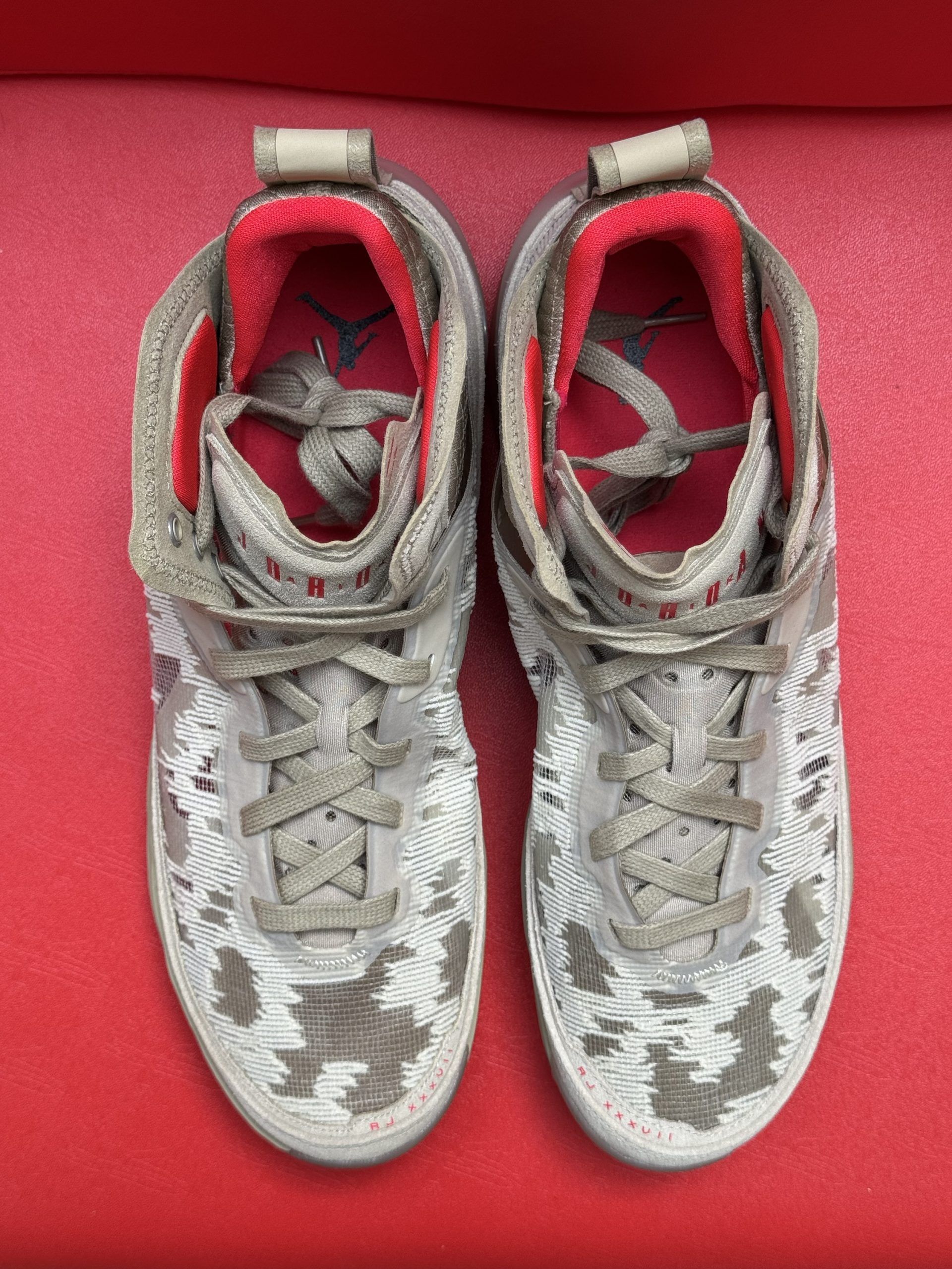 Tan and white Jordan basketball shoes with pink accents on a red surface. Marked 