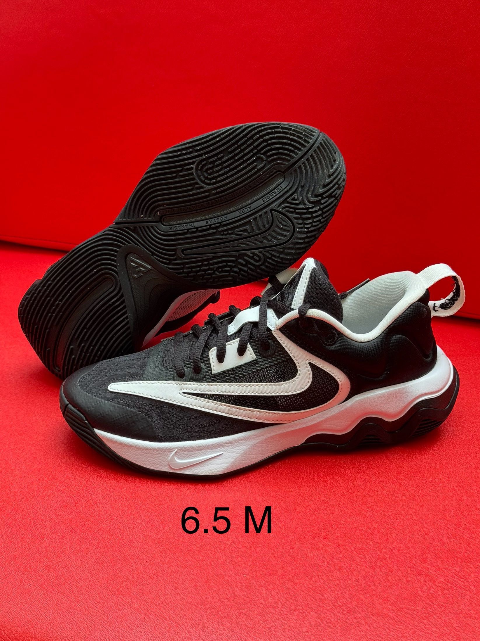 Black and white athletic shoes on a red surface; size 6.5 M.